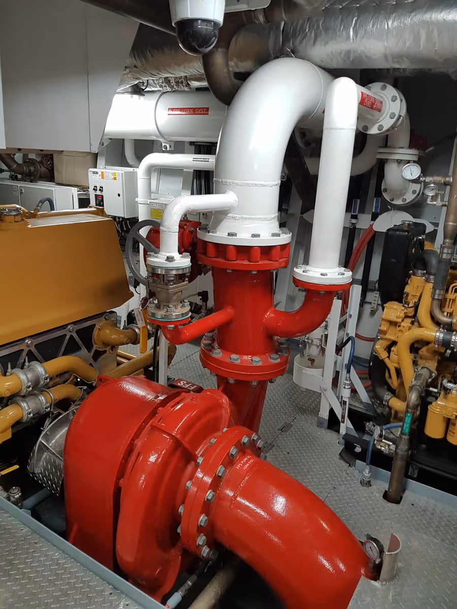 Industrial pump system with red and white large pipes and valves in a mechanical room.