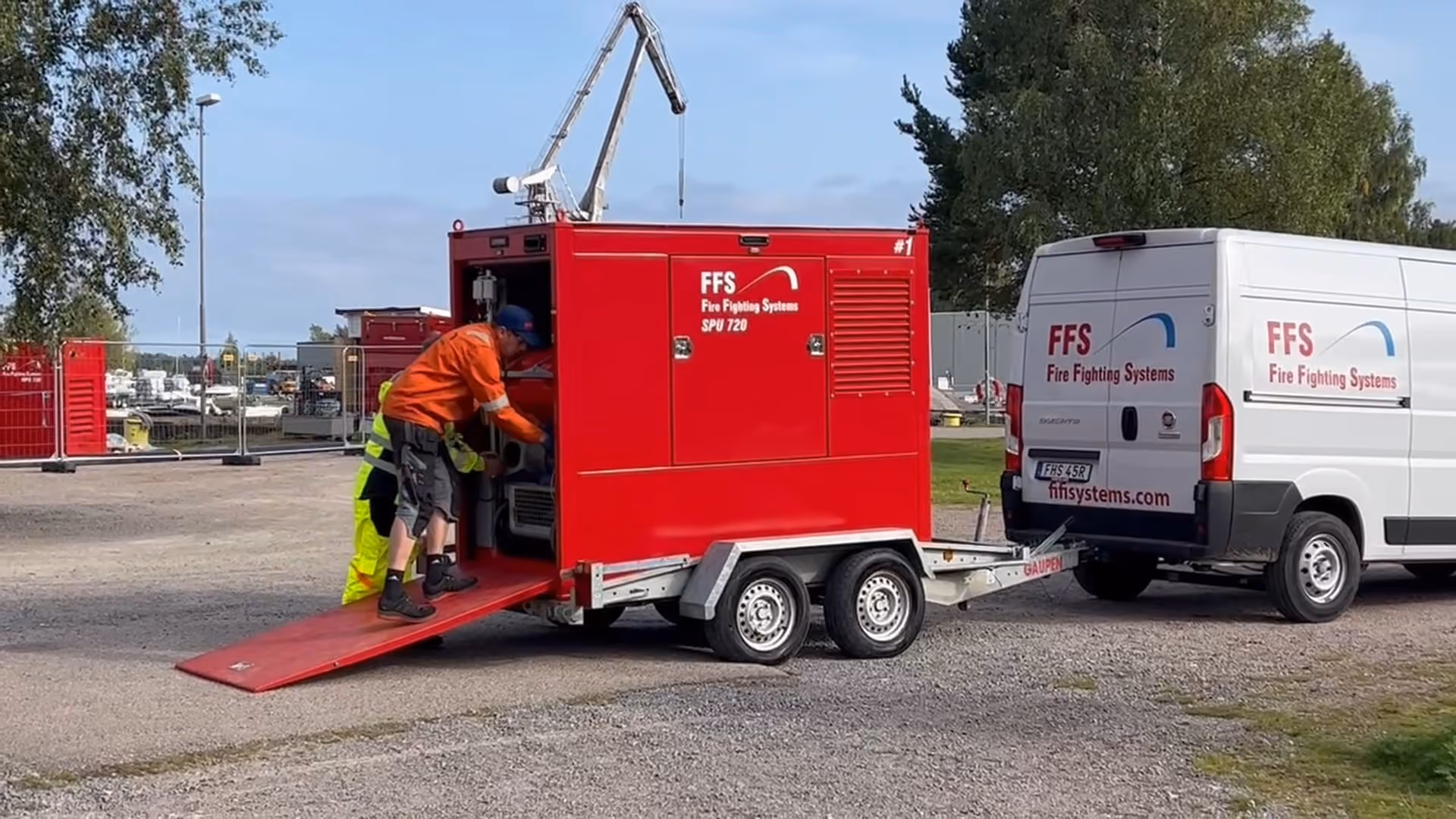 Two men working on a red fire fighting trailer attached to a white van with FFS logos.