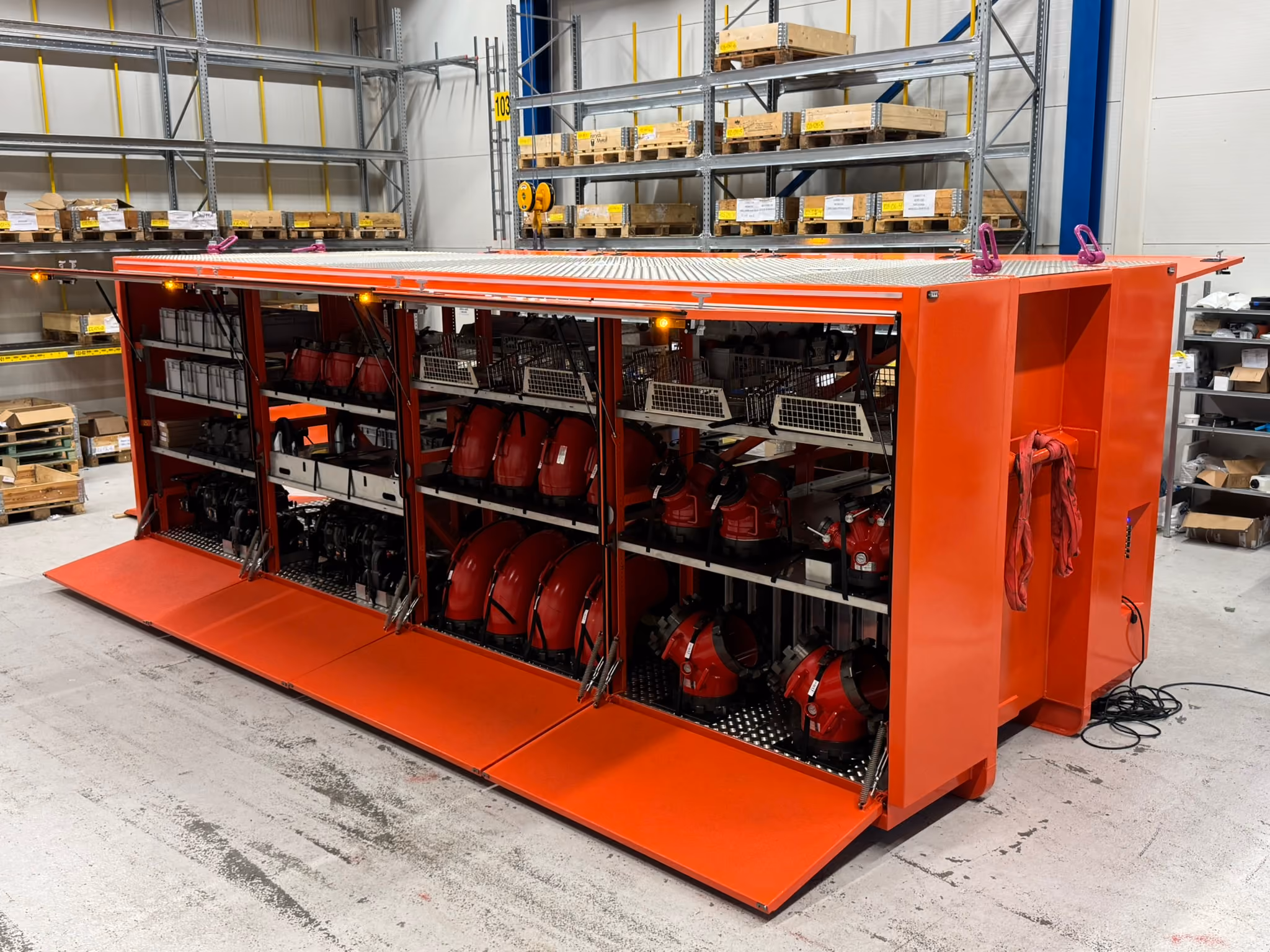 Large red metal storage unit with open compartments holding red industrial equipment in a warehouse.