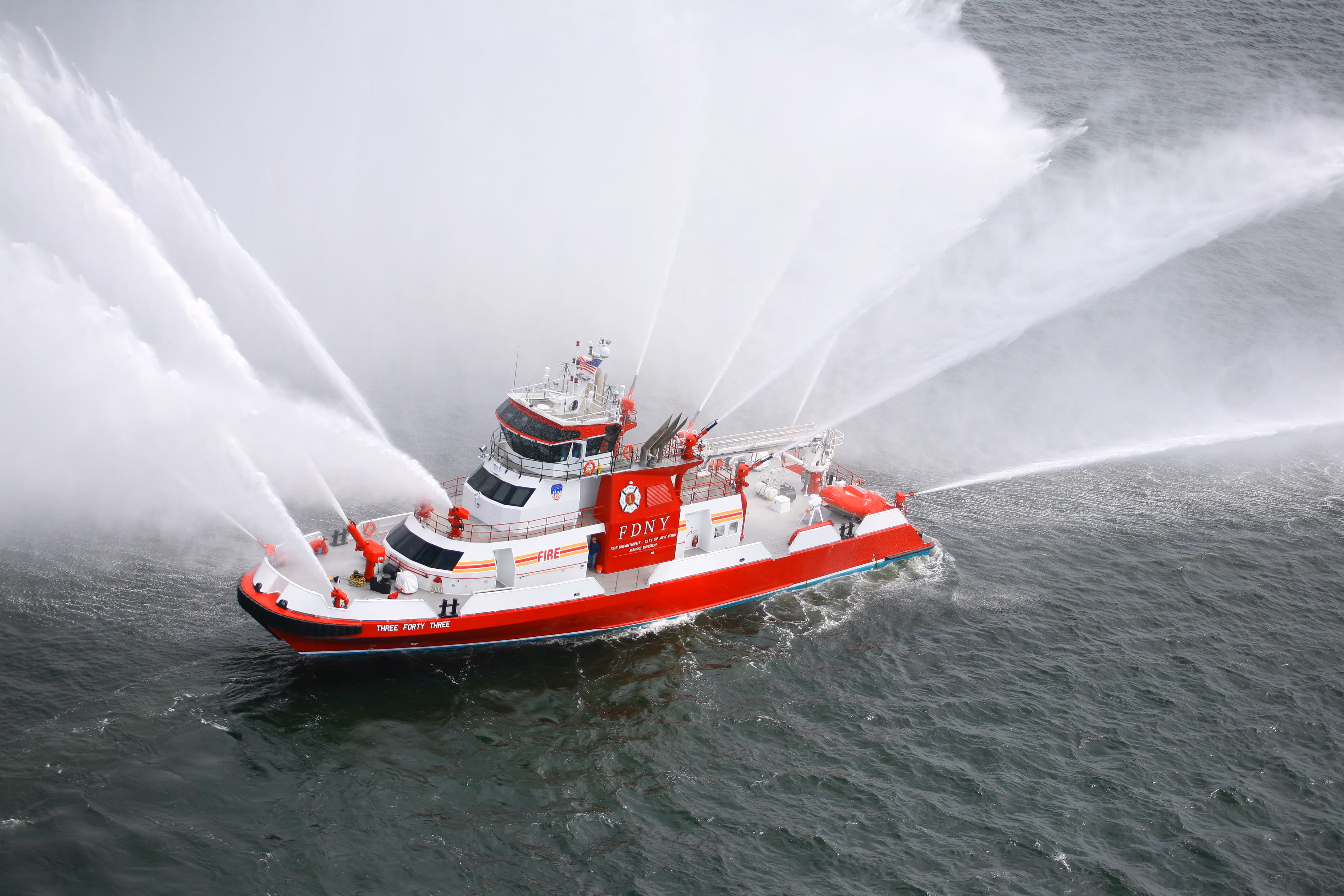 FDNY fireboat spraying multiple water streams over water during a firefighting demonstration.