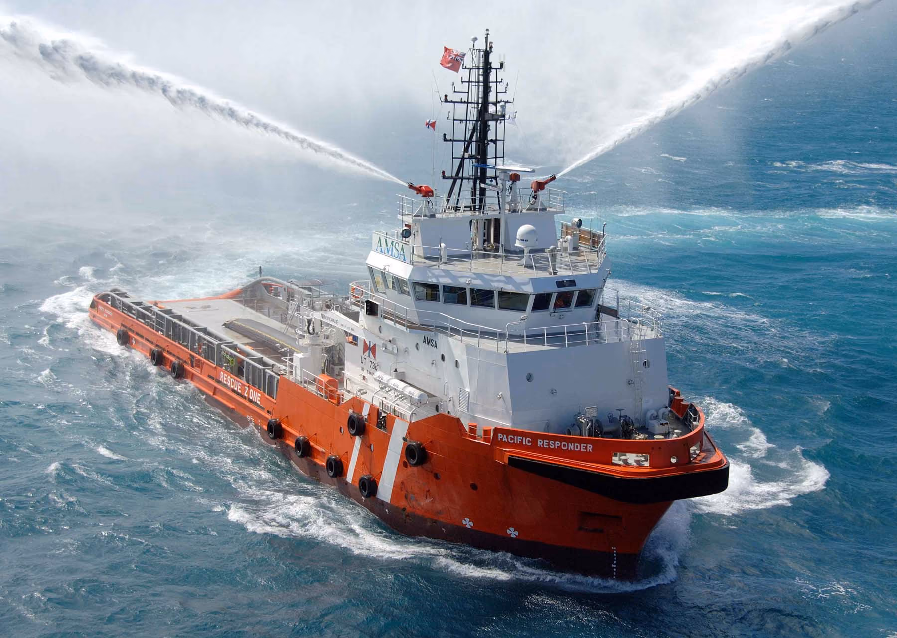Red and white rescue ship named Pacific Responder spraying water over the ocean surface.