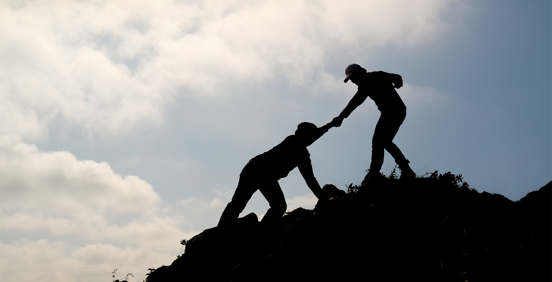 Silhouette of one friend reaching out to pull another up, representing offered support