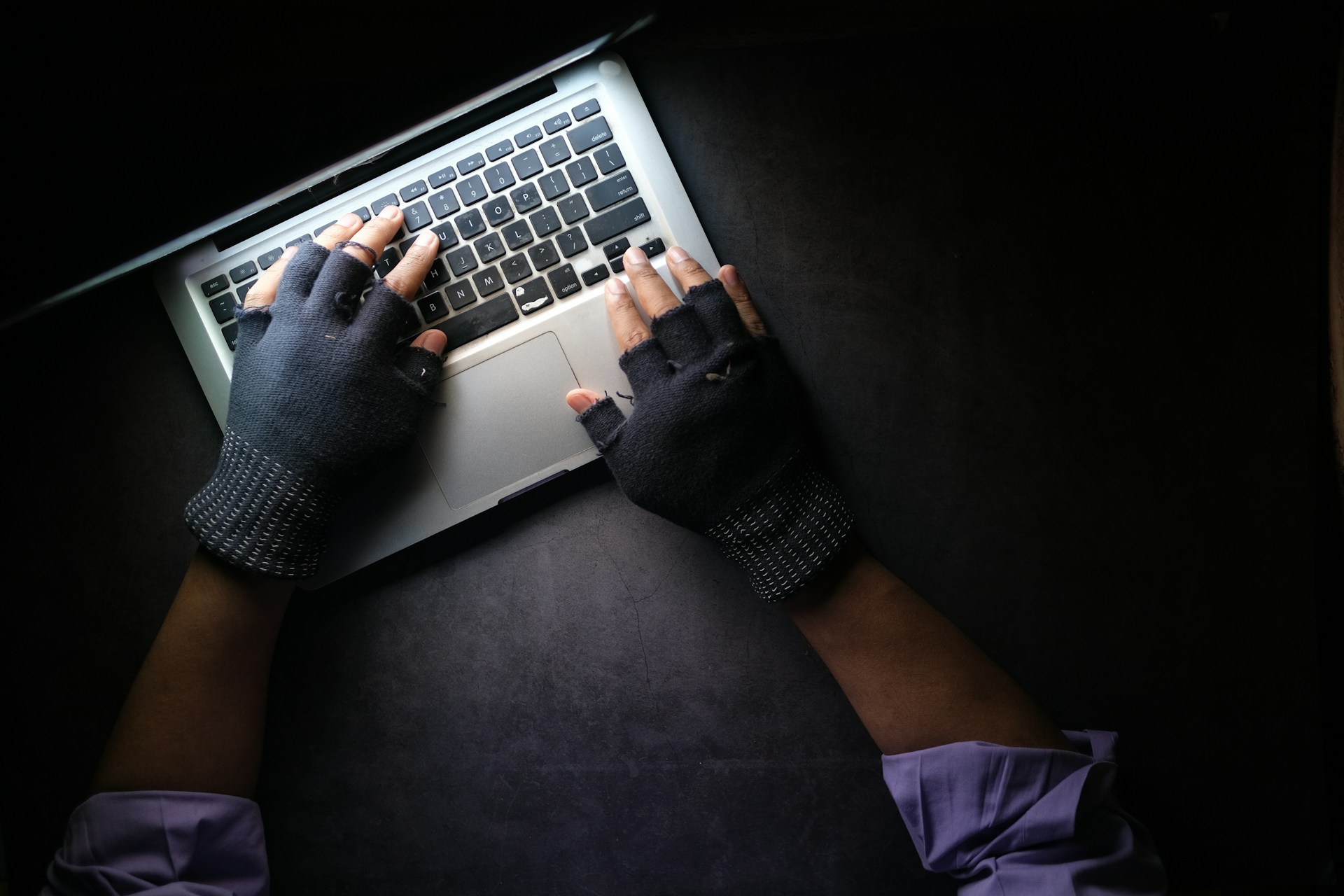 Person wearing gloves typing on laptop representing cybersecurity risk and digital workflow security in wealth management
