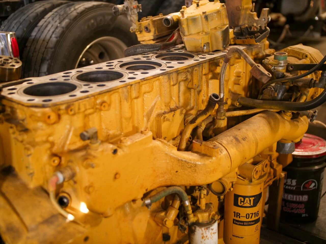 Engine repair with CAT diesel engine block exposed, showing cylinder bores and 1R-0716 oil filter during rebuild.