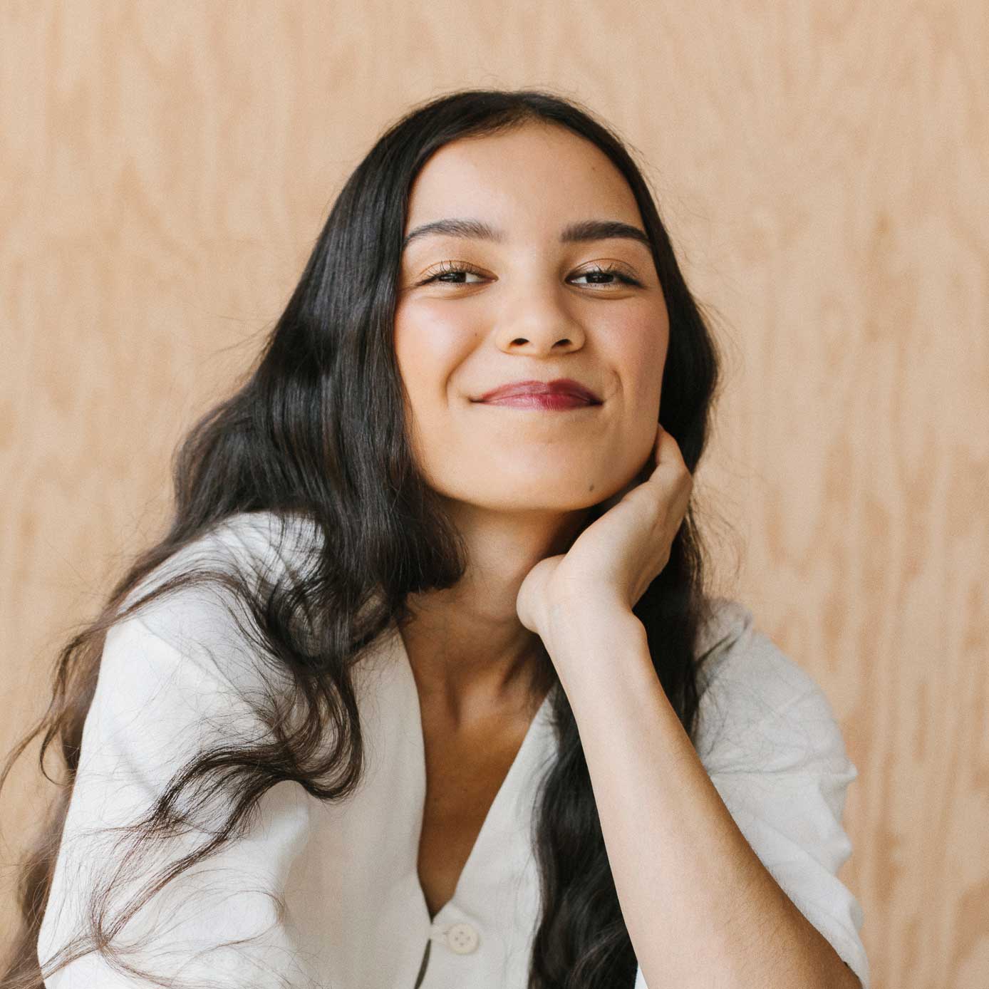 A woman poses for the camera, she smiles cheekily and leans on her hand.
