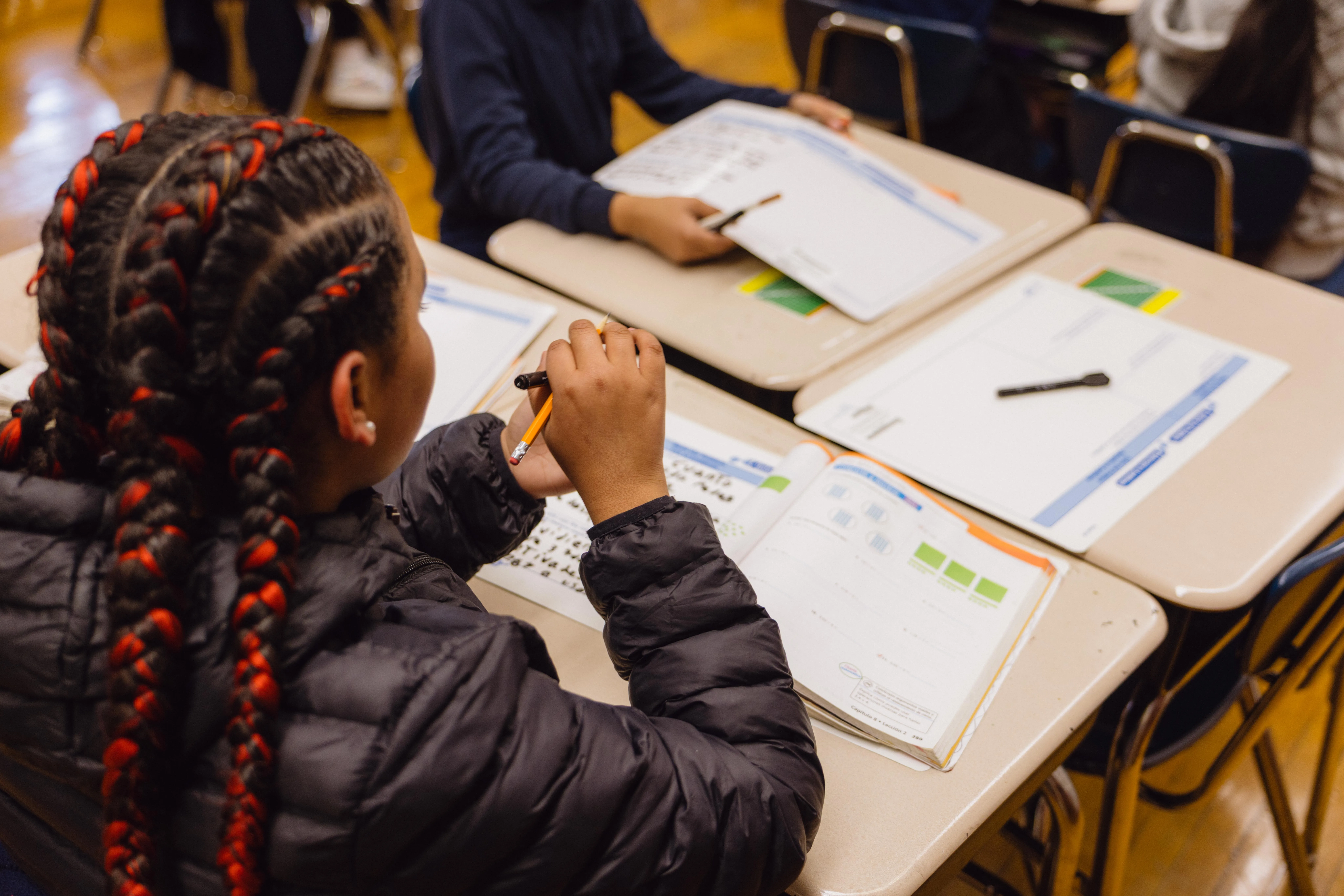 A student with braided hair works through a worksheet at a classroom desk