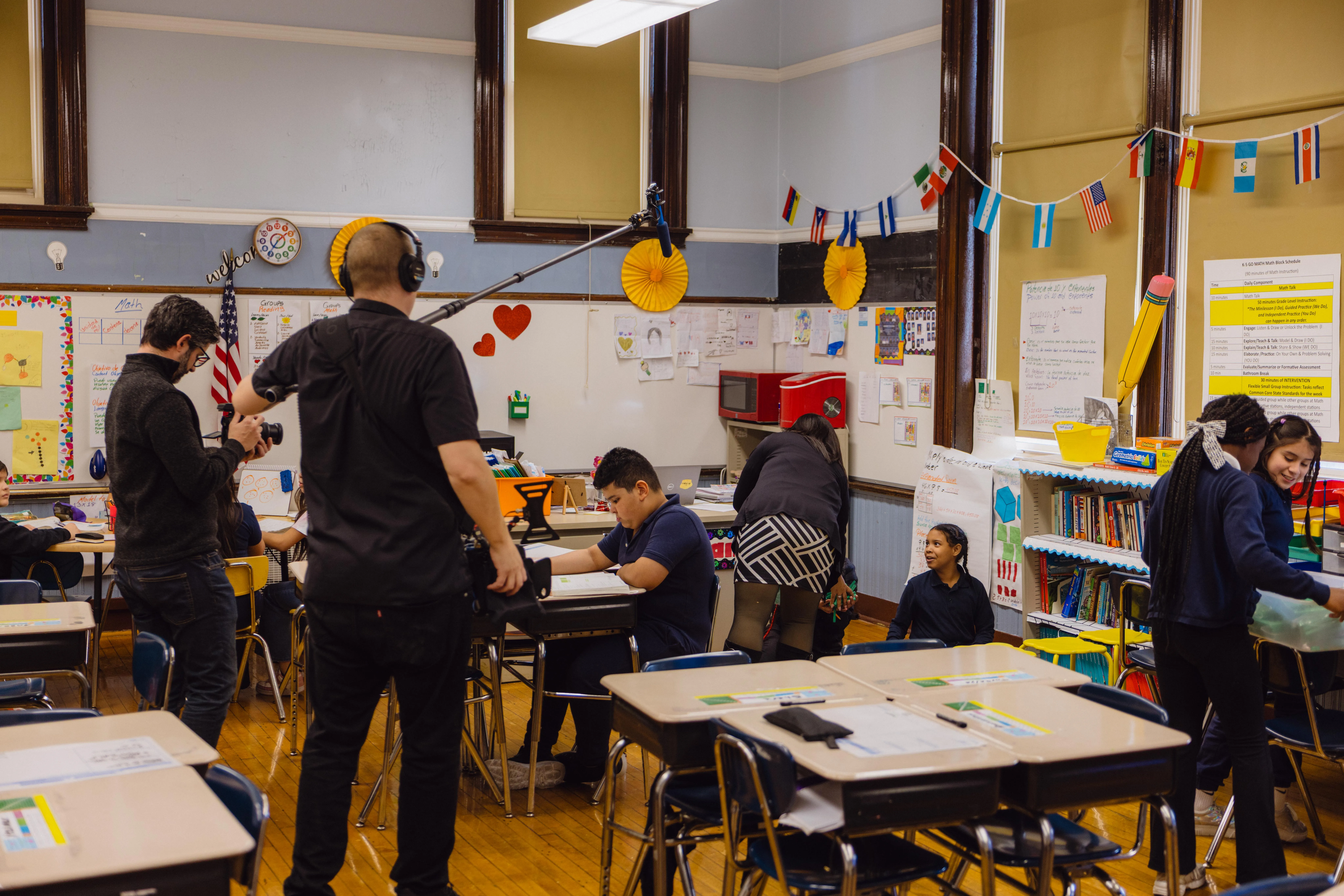 A film crew recording with a boom microphone in a classroom while students work at their desks