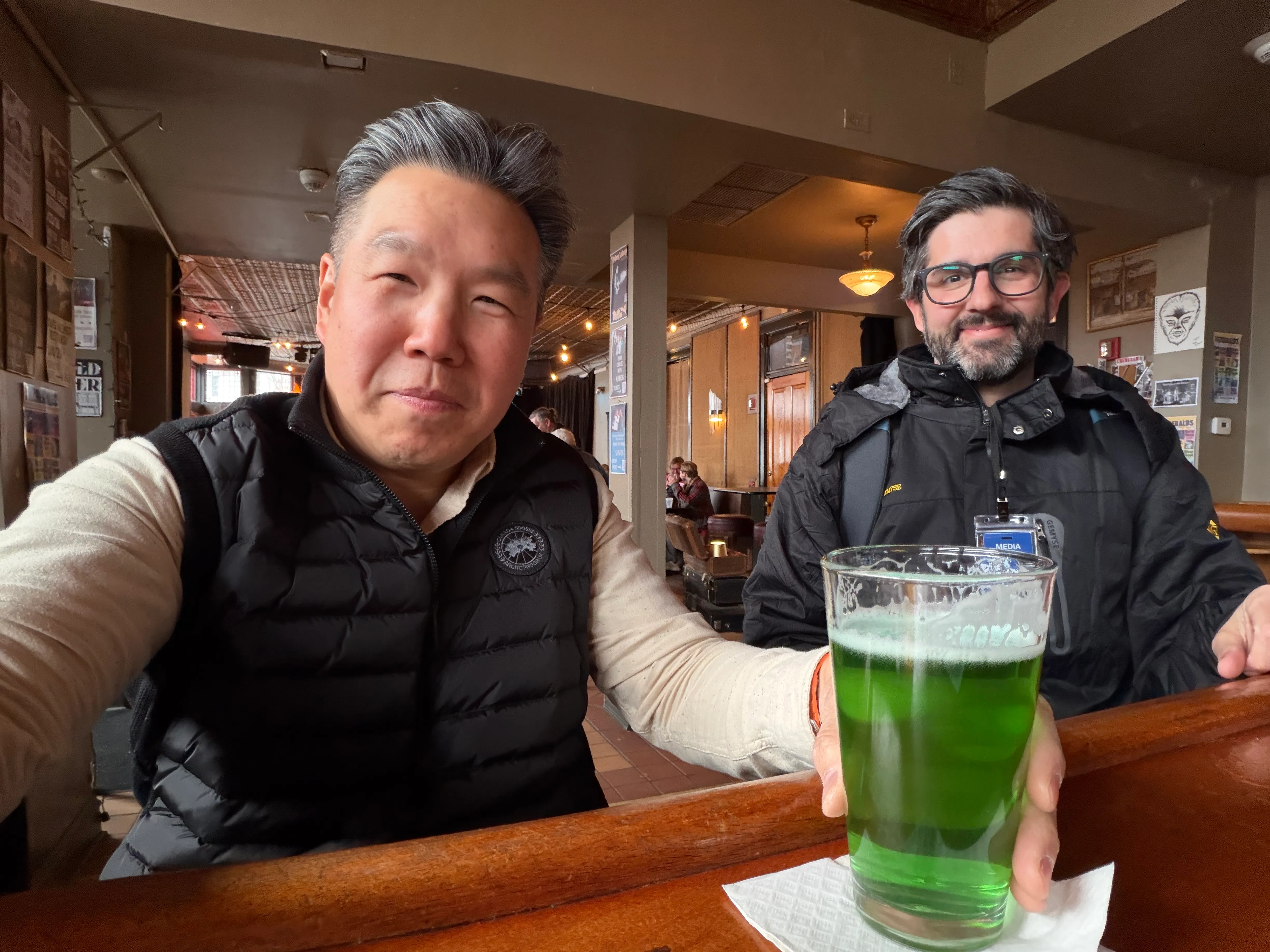 Two men at a Chicago pub, one holding up a green drink to the camera