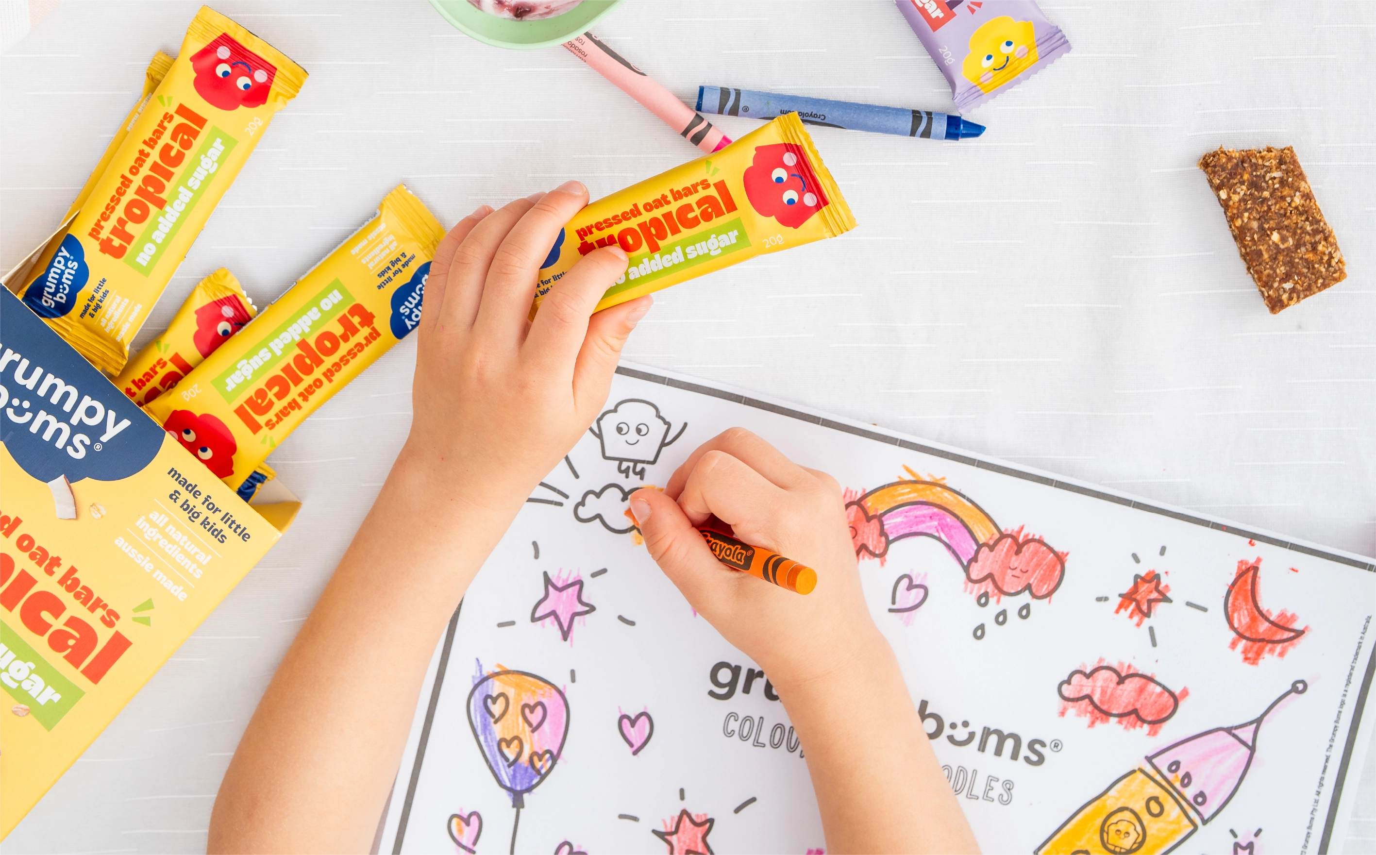 WeAreDepot Packaging Design, child’s hands with Grumpy Bums bars scattered among crayons and drawings, Australian kids snack brand packaging lifestyle shot
