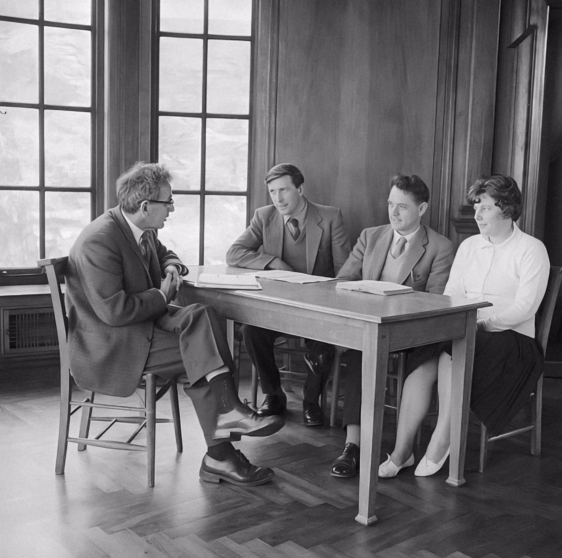 Skyscrapers seen from below against a cloudy gray sky, framed by silhouettes of tree branches.