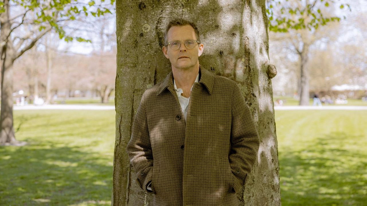 Portrait of Kresten Schultz Jørgensen standing against a tree in a sunlit park during spring.