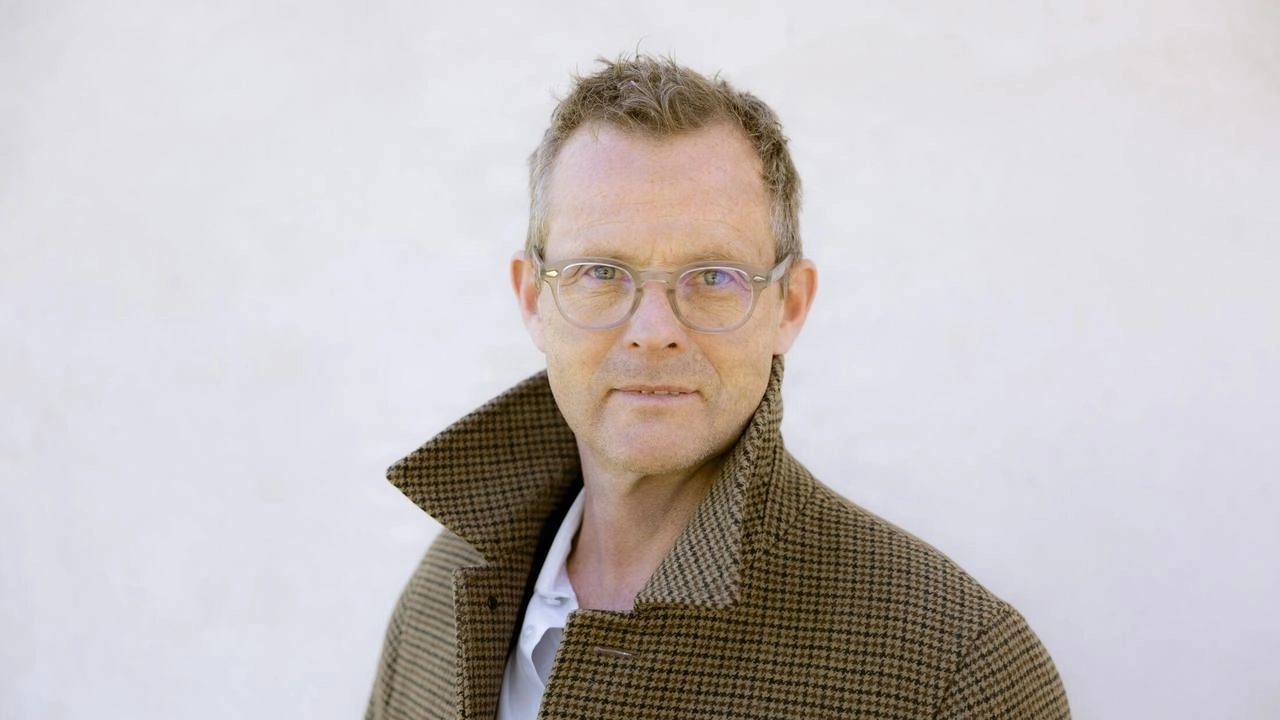Portrait of Kresten Schultz Jørgensen wearing glasses and a brown coat against a light background.