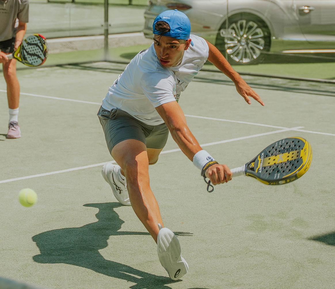 Male paddle tennis player lunging forward to hit a ball with a paddle on an outdoor court.