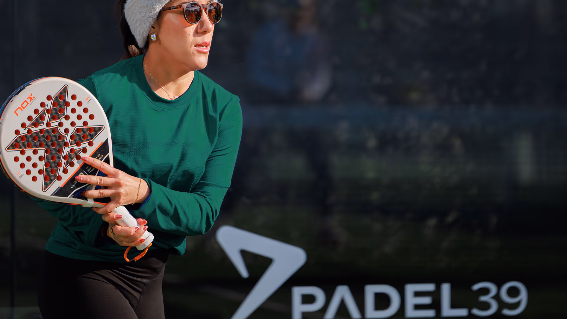Man wearing white sportswear and a cap walking on a padel court with a racket bag over his shoulder.