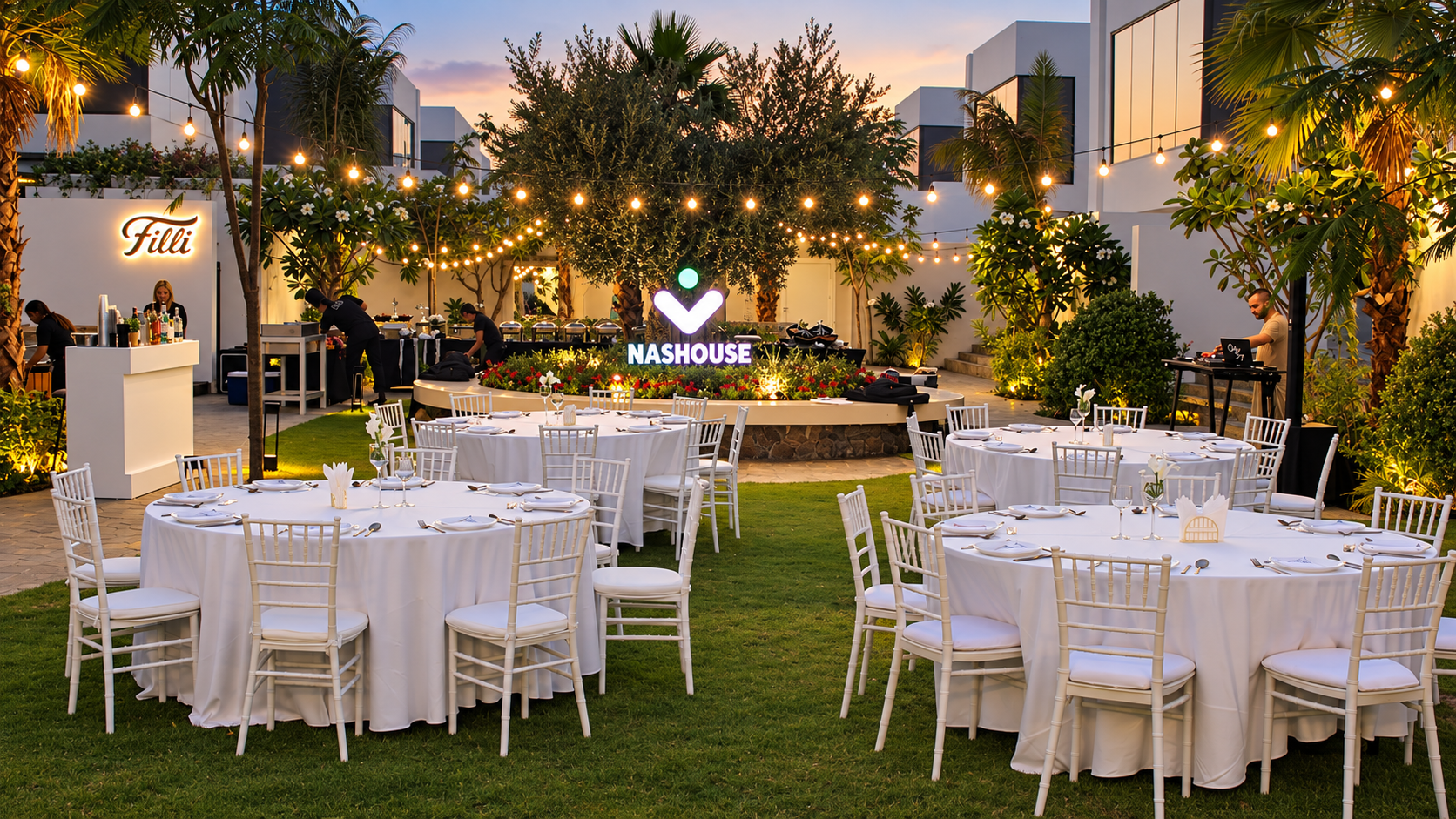 An elegant outdoor dinner in the Nas House garden, with white table settings and glowing string lights.