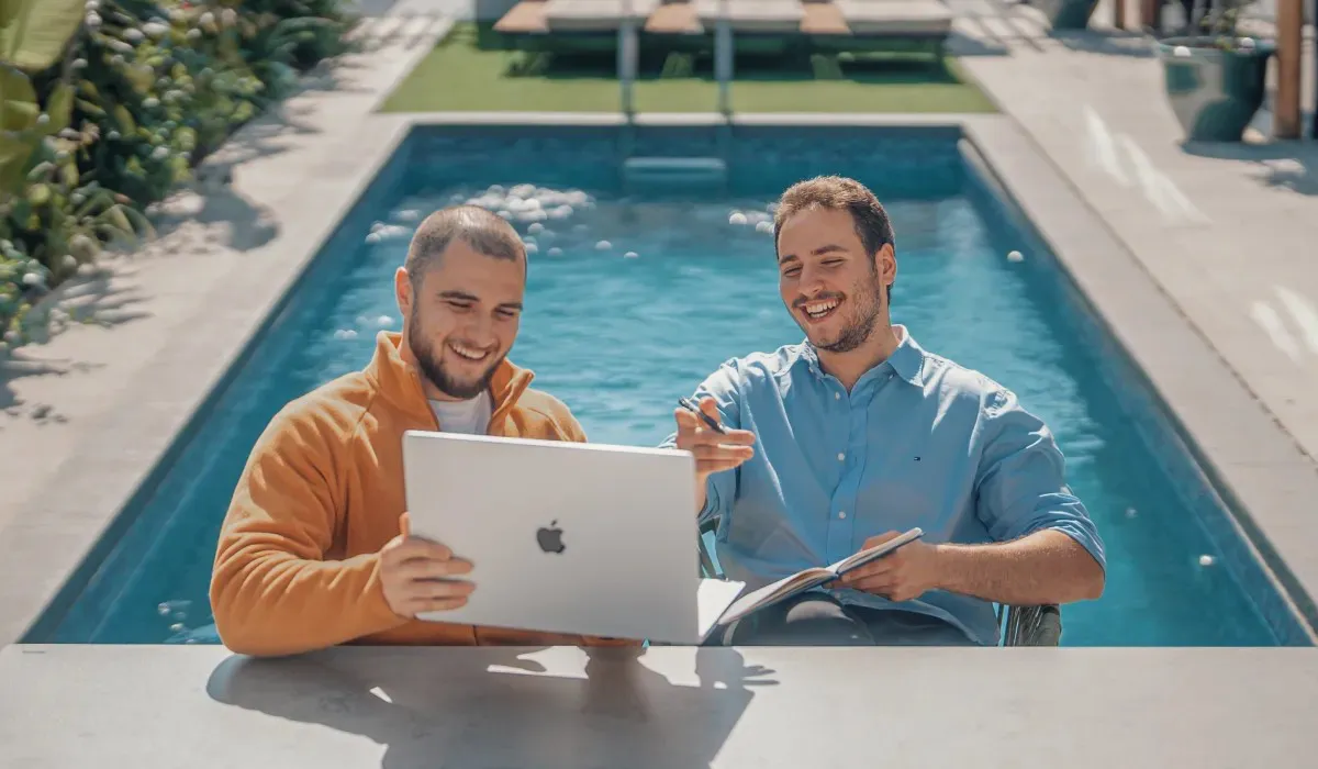 Two colleagues working on a laptop beside the pool