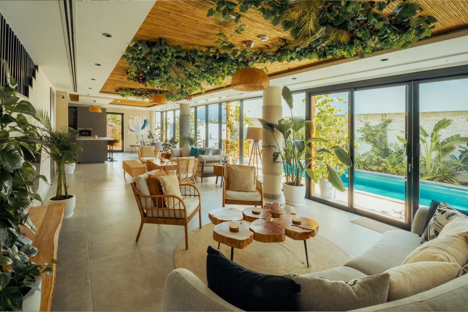 A bright lounge with plants hanging from the ceiling, opening onto a pool