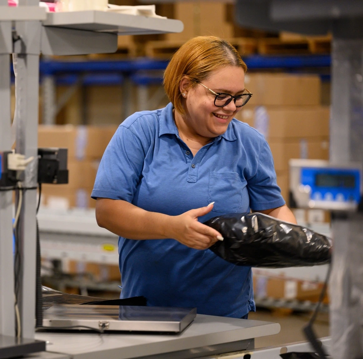 A smiling warehouse worker holding a black package.