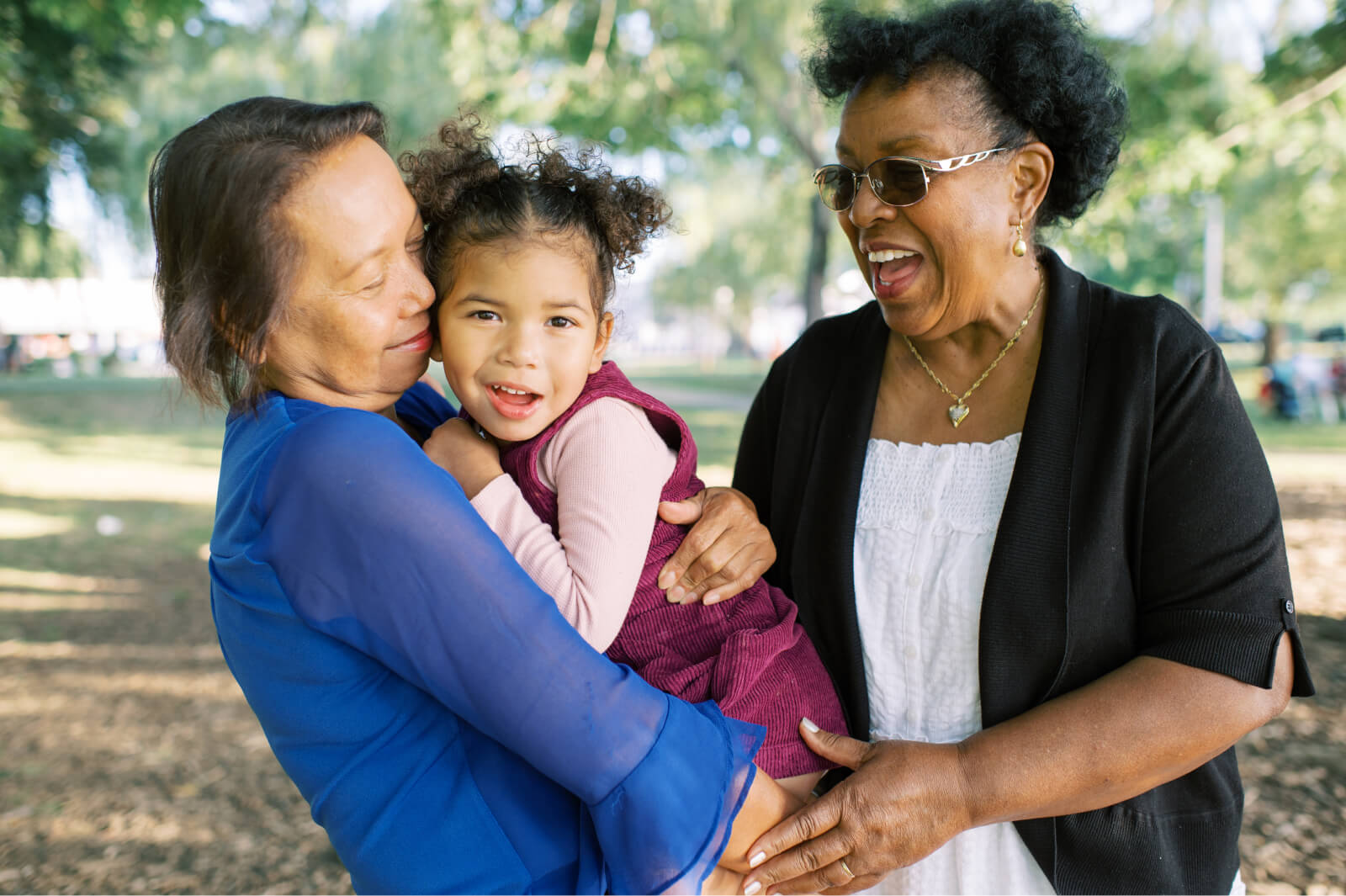 Two Grandmothers Hugging And Laughing With Granddaughter Together
