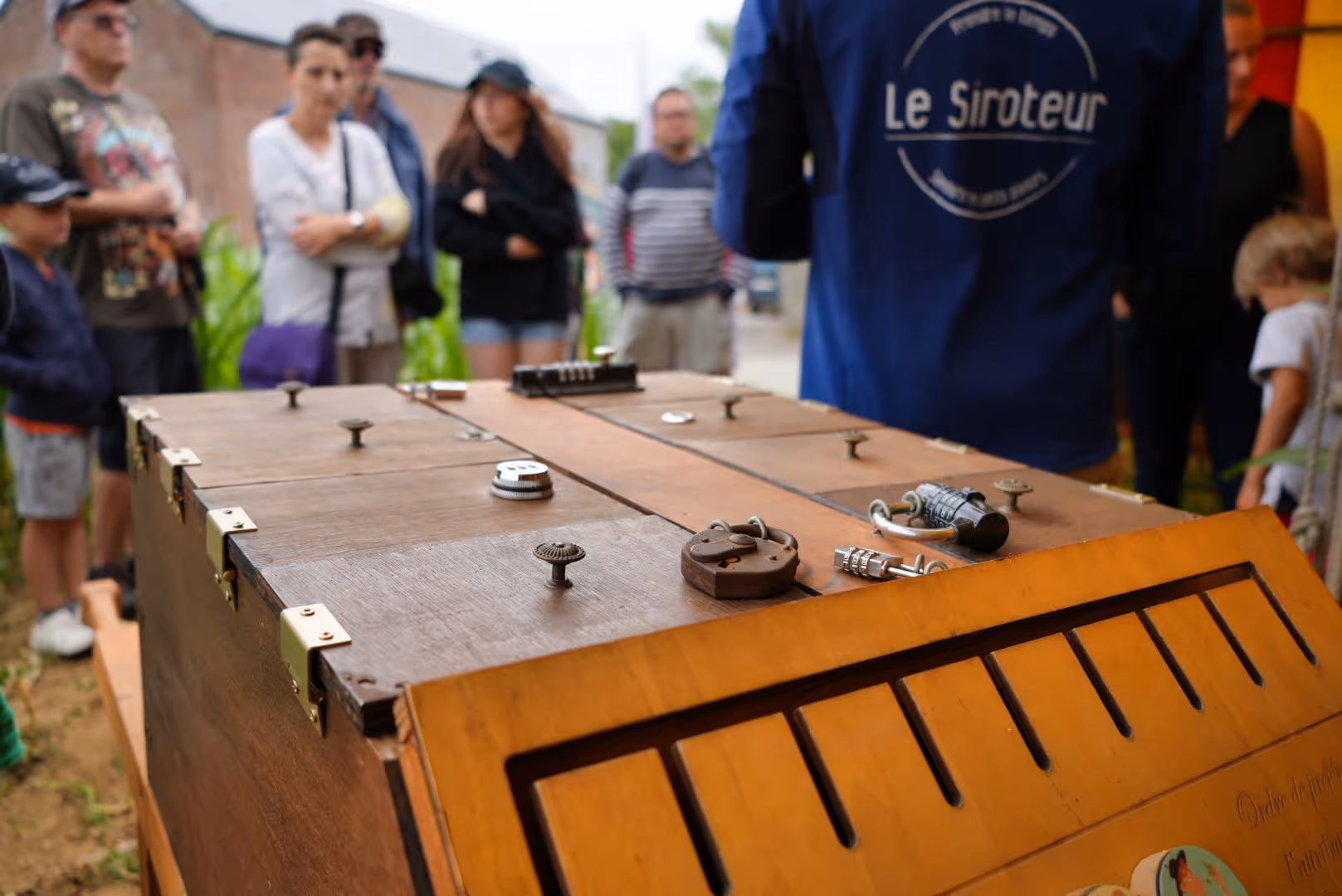 Boîte en bois avec plusieurs cadenas, devant un groupe de personnes lors d'une démonstration.