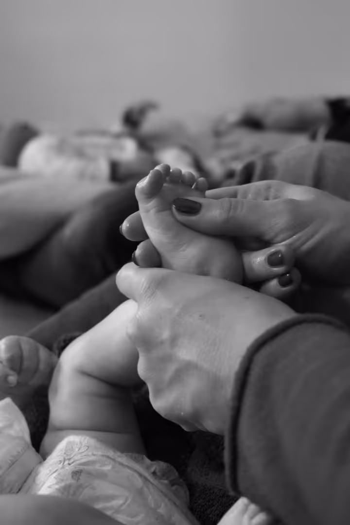 Mains tenant et massant le pied d'un bébé couché, en noir et blanc.