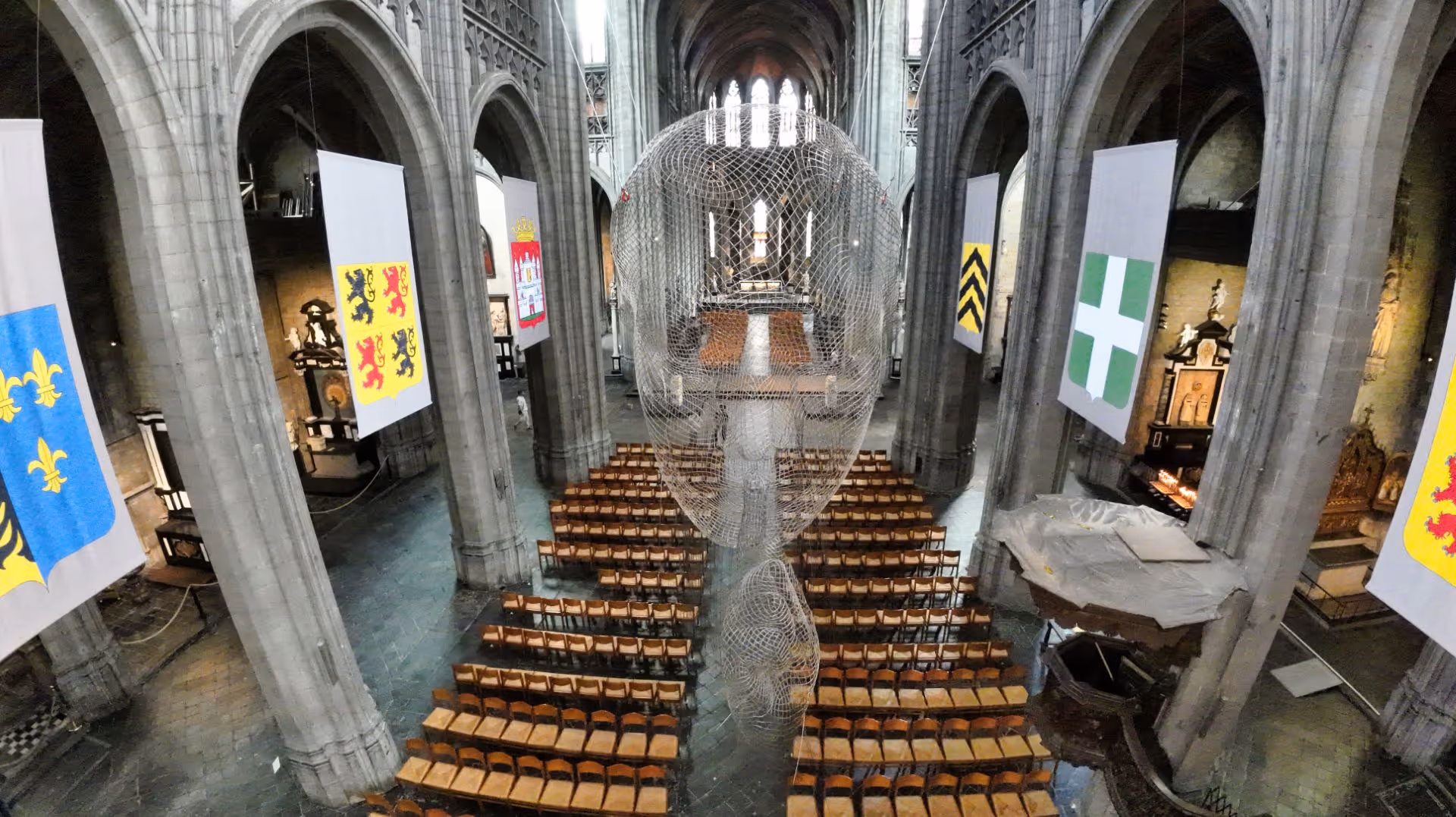 Intérieur d'une cathédrale gothique avec une grande sculpture filaire de tête suspendue au centre.