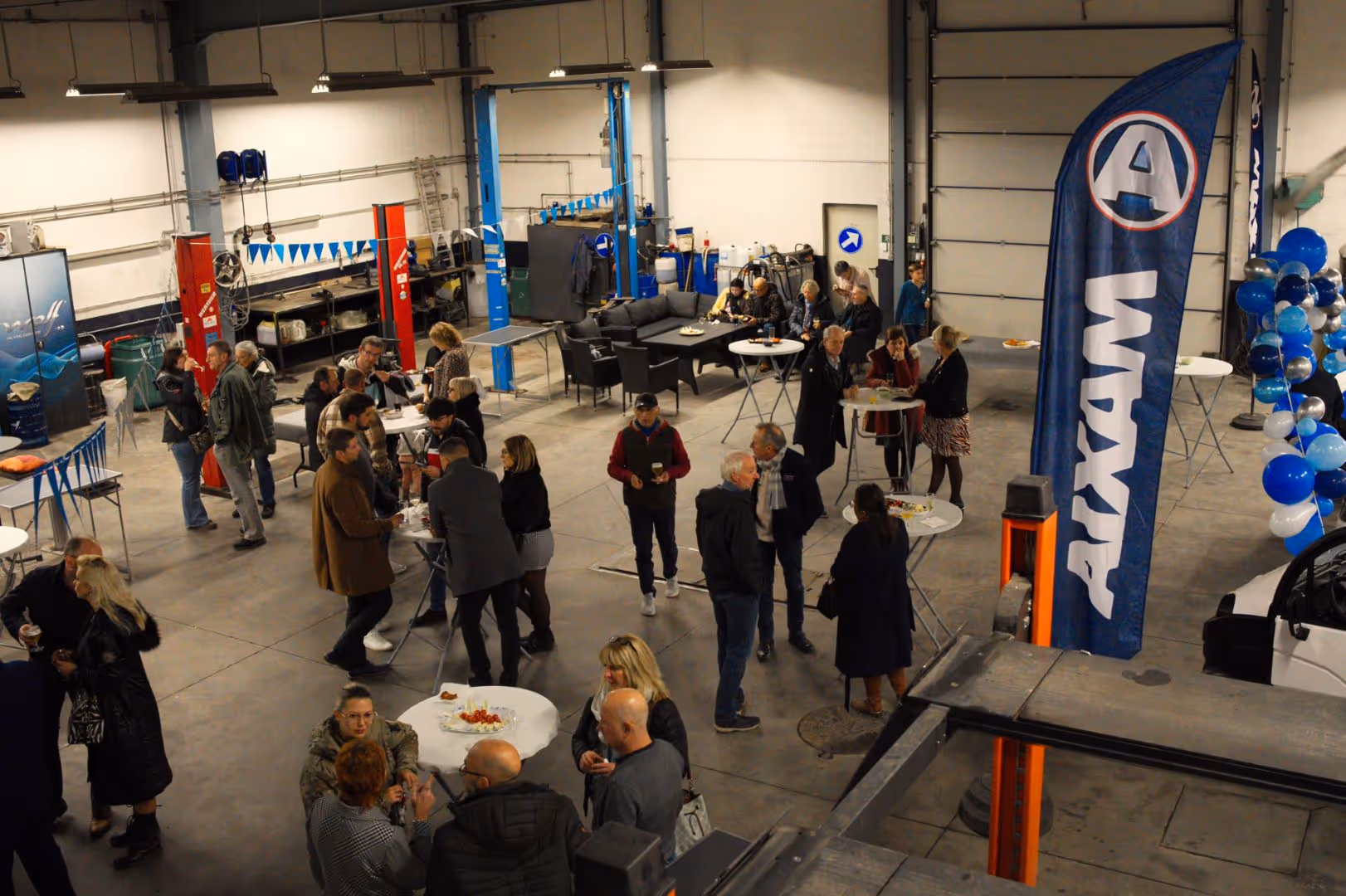 Groupe de personnes discutant debout autour de tables dans un grand espace industriel décoré pour un événement.