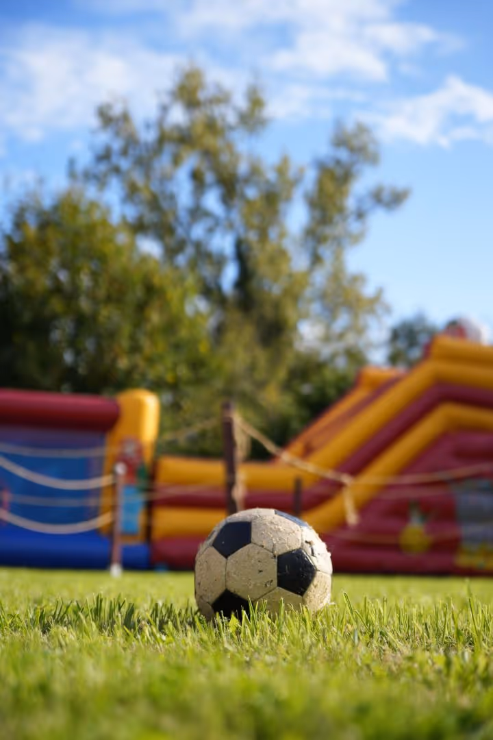 Un ballon de football noir et blanc sur l'herbe avec un château gonflable coloré en arrière-plan.