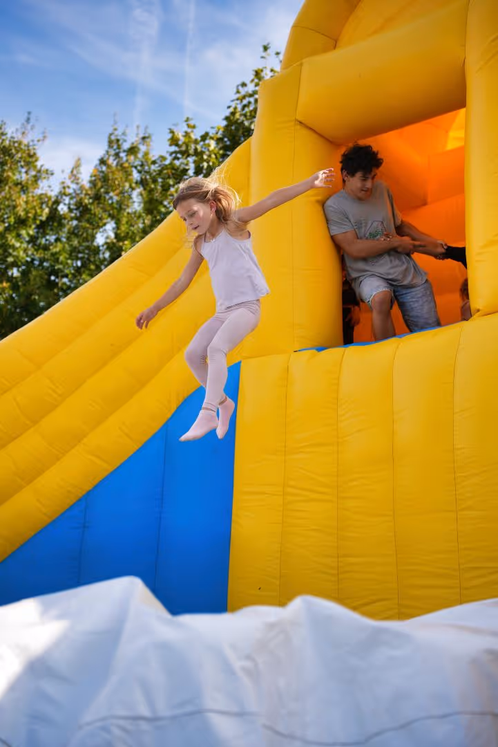 Une fille saute d'un château gonflable jaune et bleu sous un ciel bleu par temps ensoleillé.