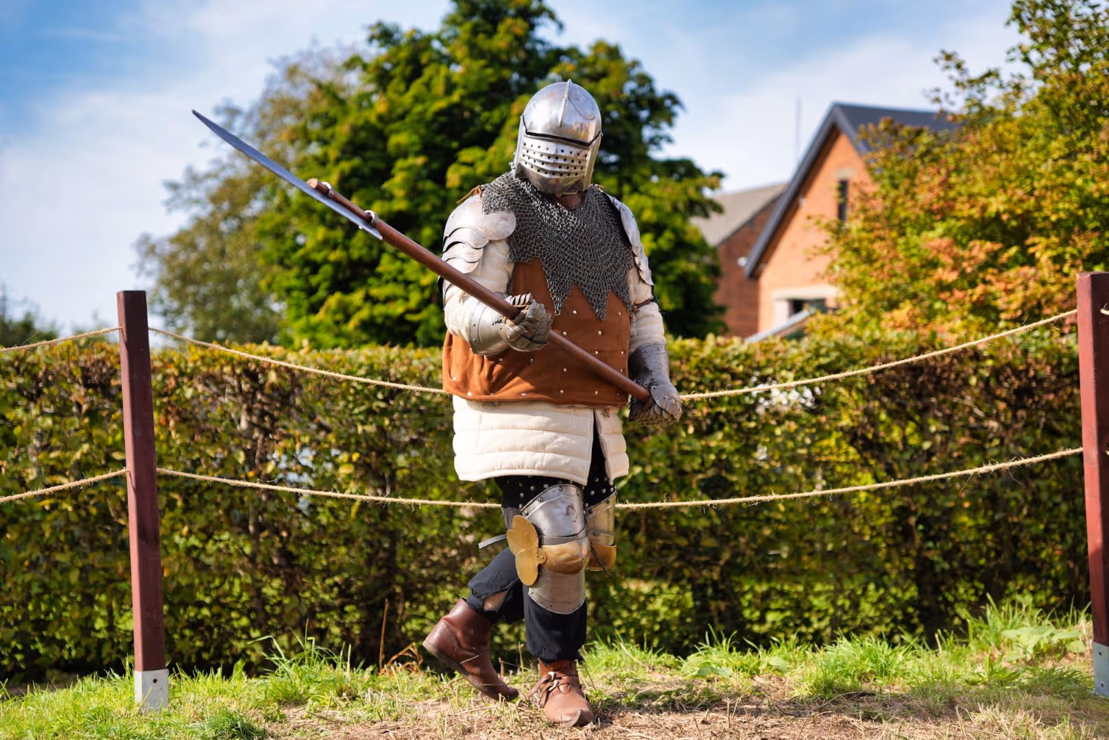 Un chevalier en armure médiévale tenant une lance avec un casque à visière dans un cadre extérieur.