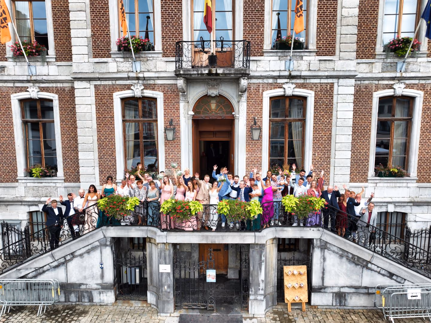 Groupe de personnes habillées élégamment posant sur les escaliers devant un bâtiment historique en brique.