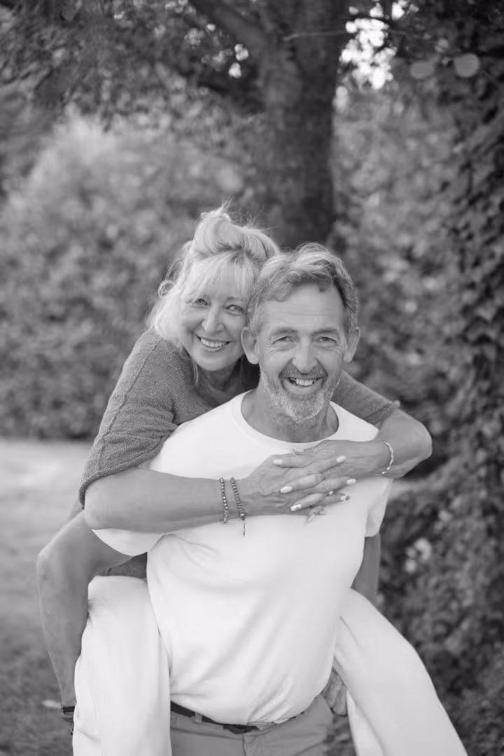 Couple souriant avec femme faisant un câlin dans le dos d'un homme dans un jardin.
