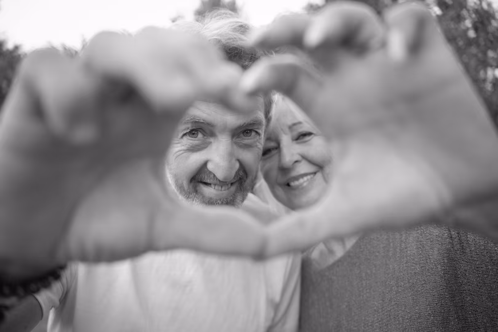 Couple souriant regarde à travers un cœur formé par leurs mains devant eux.