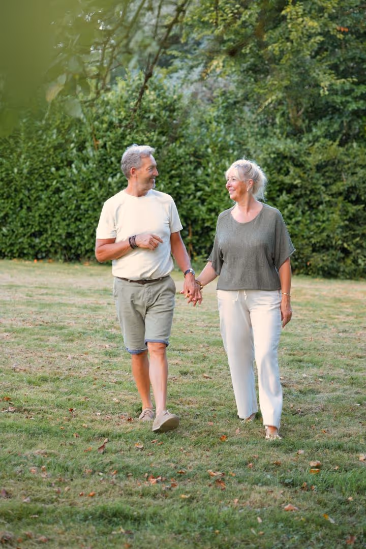 Un couple senior se tenant la main en marchant dans un parc verdoyant et souriant.