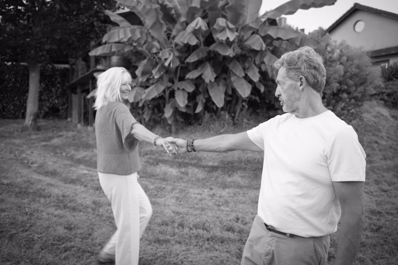 Un homme et une femme se tiennent la main dans un jardin, souriant et regardant l'un l'autre.