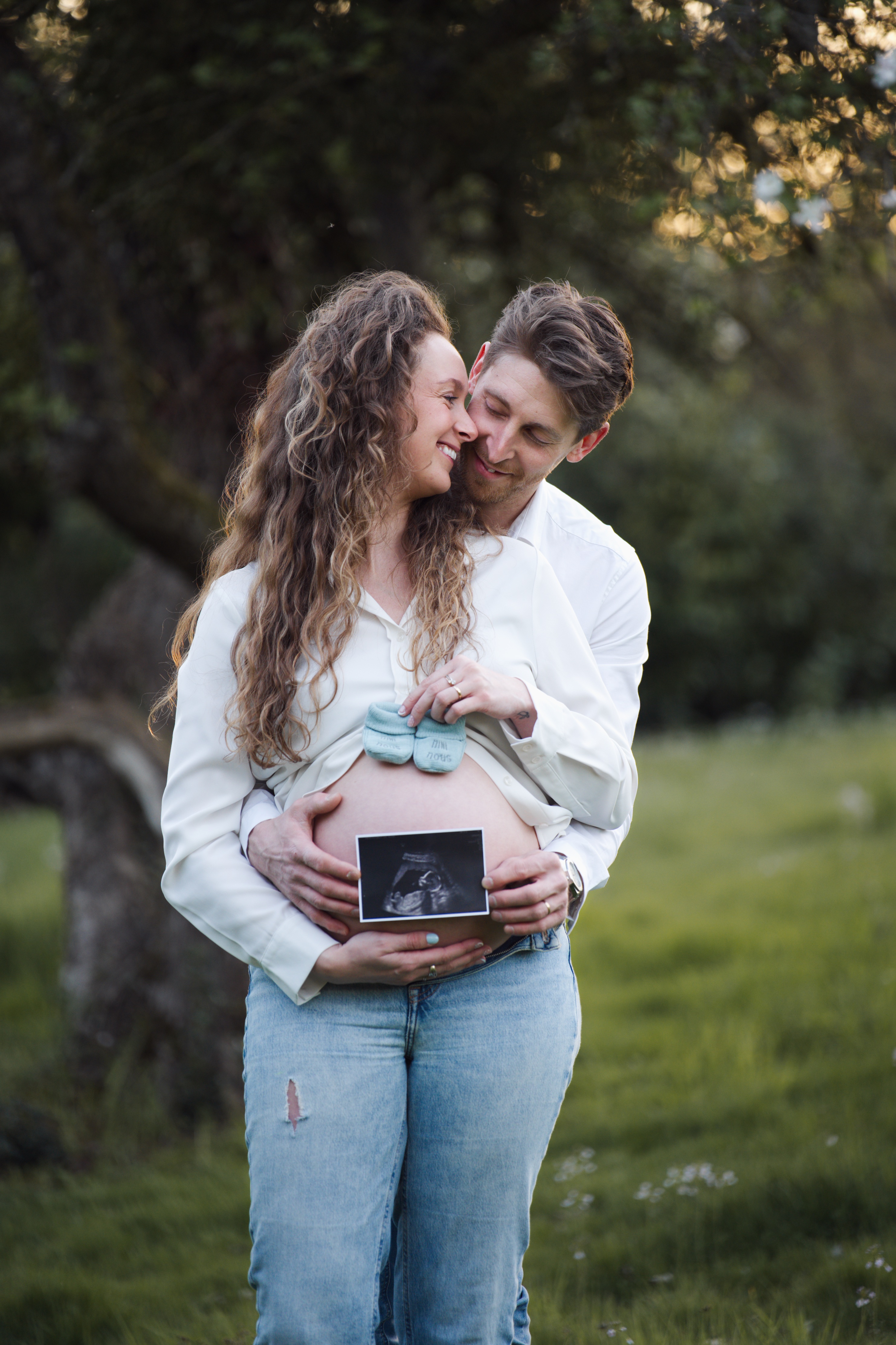 Couple souriant en plein air, homme tenant bébé échographie et chaussons sur ventre de femme enceinte.