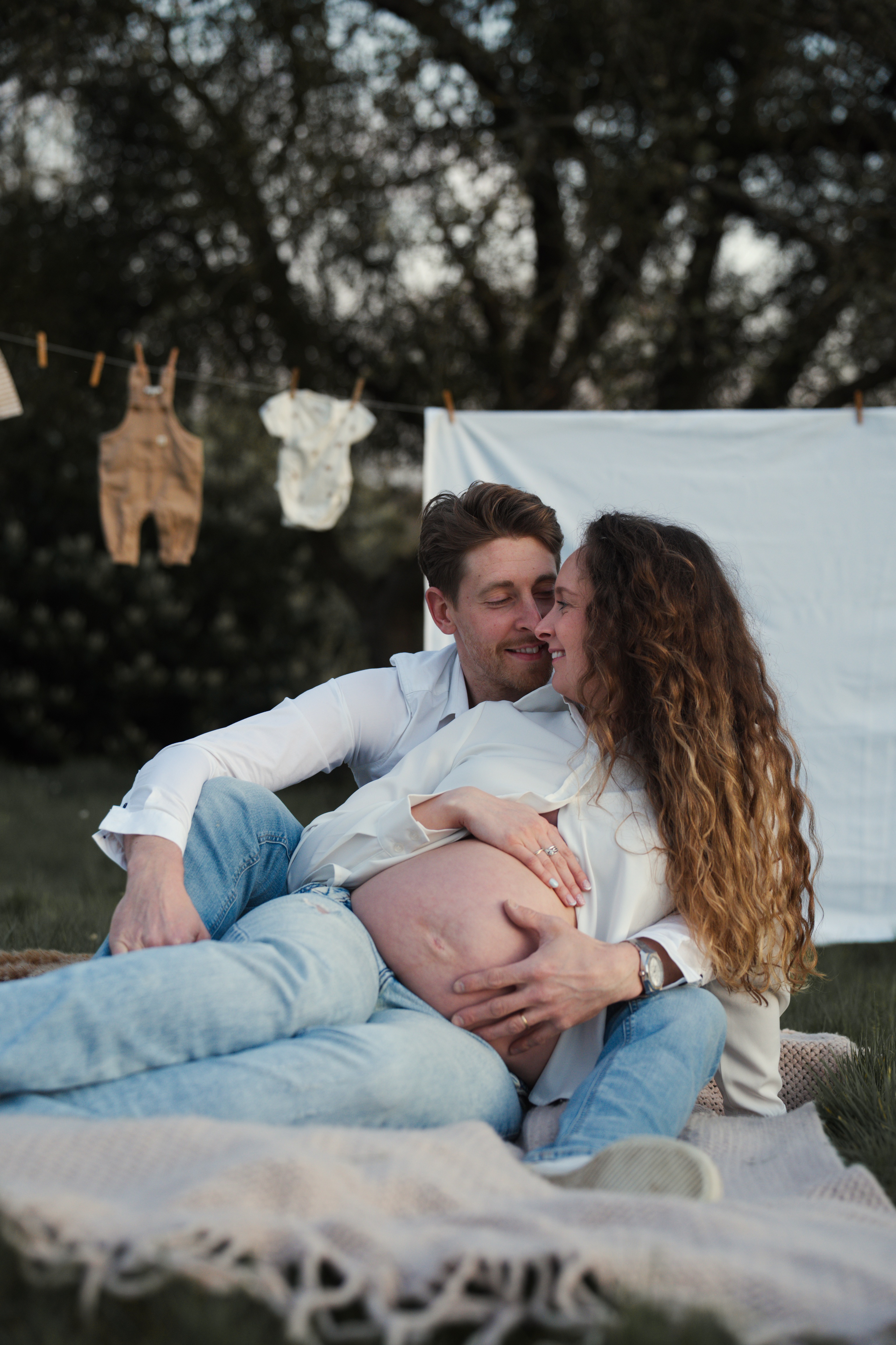 Couple en plein air, homme embrassant femme enceinte allongée sur une couverture dans un jardin.
