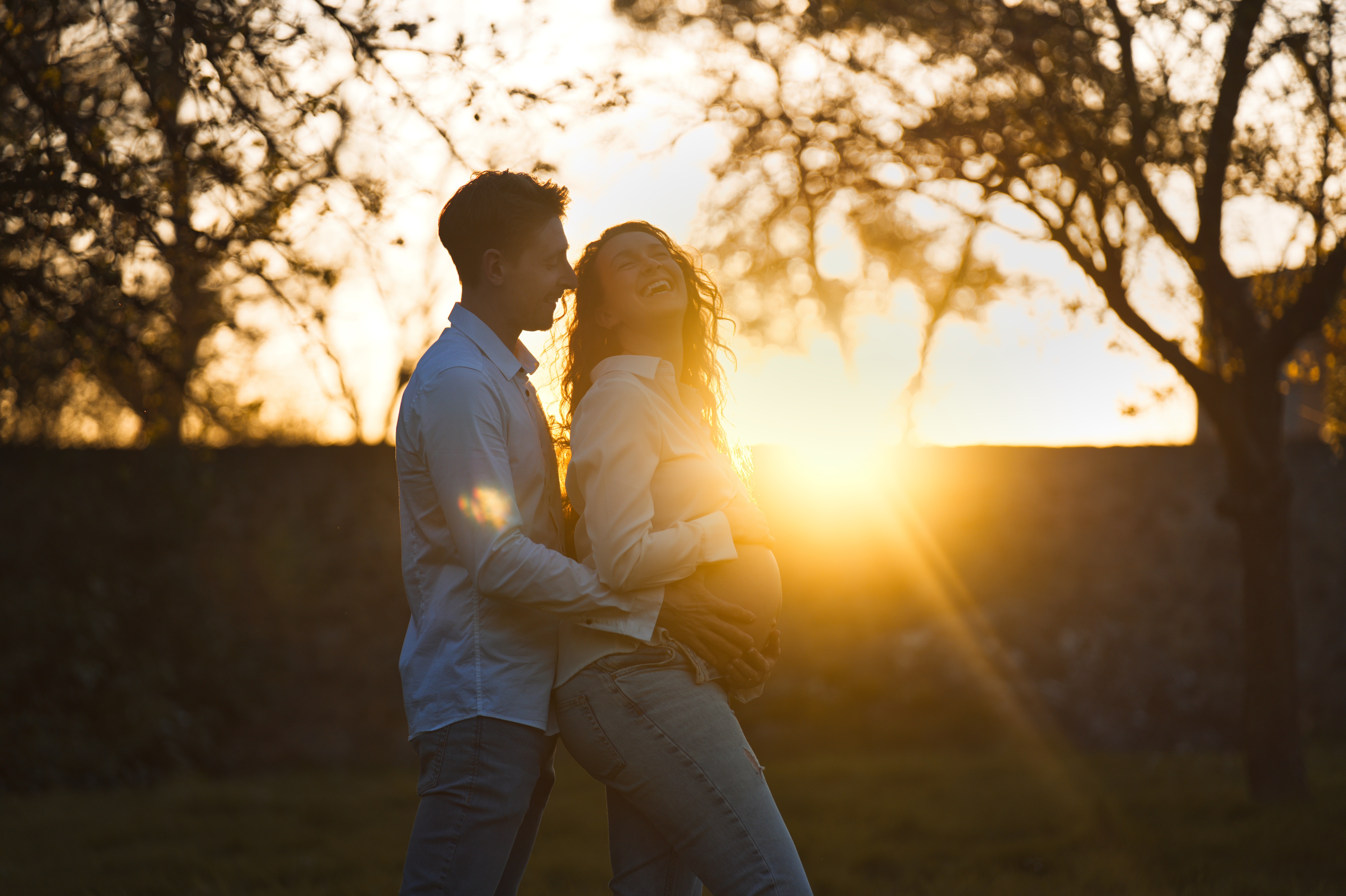 Couple heureux en extérieur au coucher du soleil, l'homme tient le ventre de la femme enceinte.