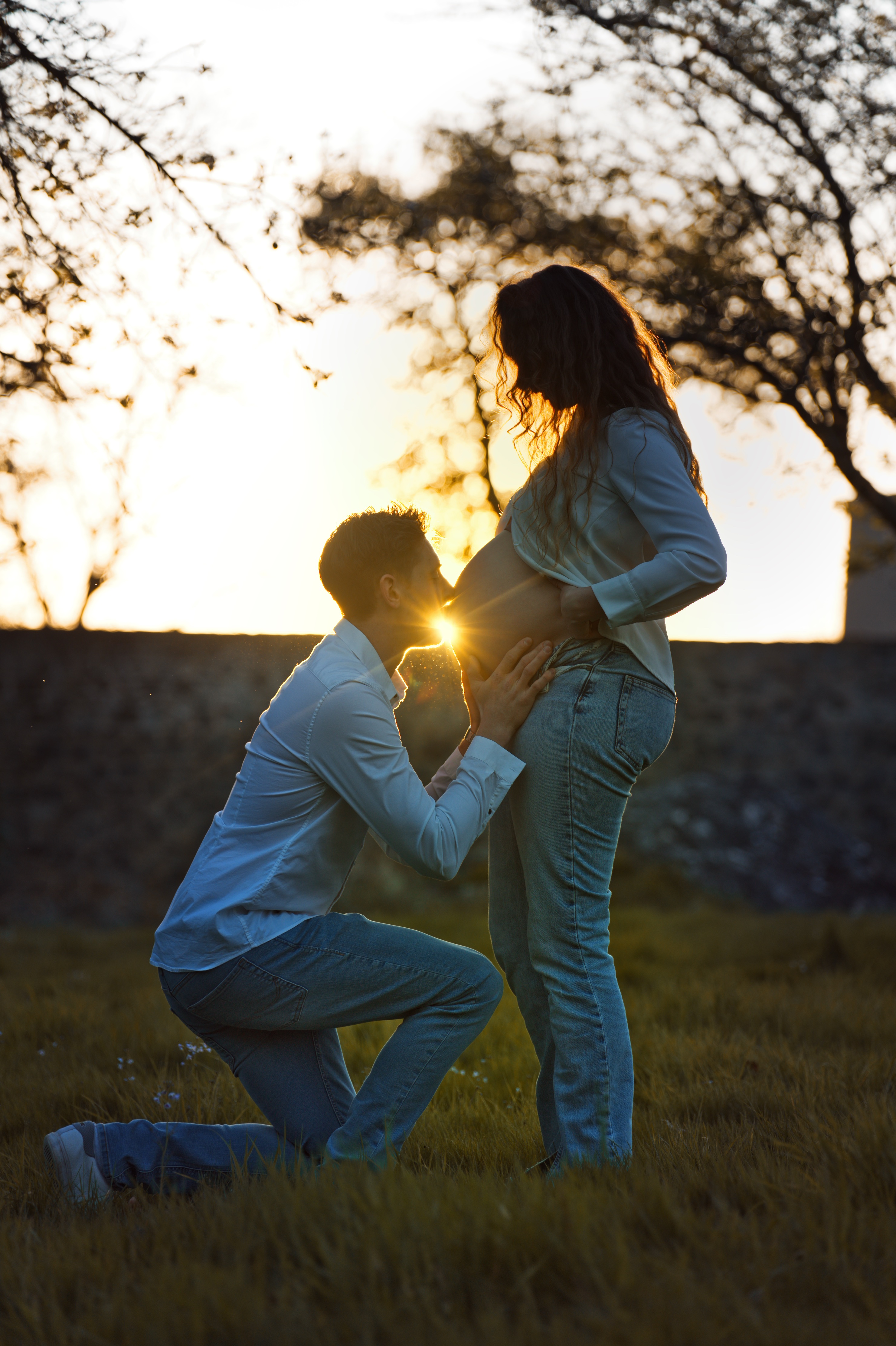 Un homme embrasse le ventre d'une femme enceinte au coucher du soleil dans un champ.