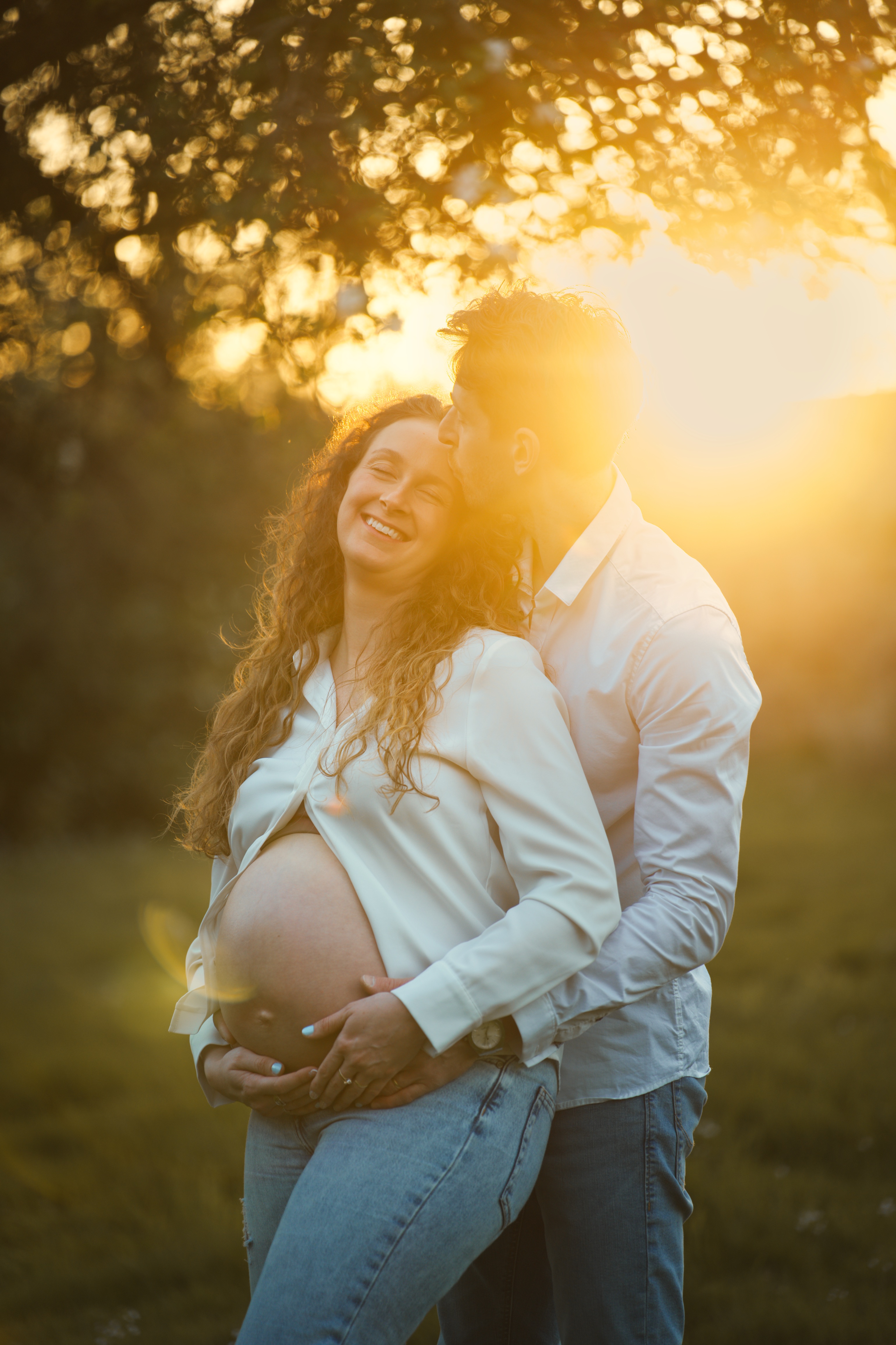 Couple en plein air, homme embrassant femme enceinte souriante au coucher du soleil.
