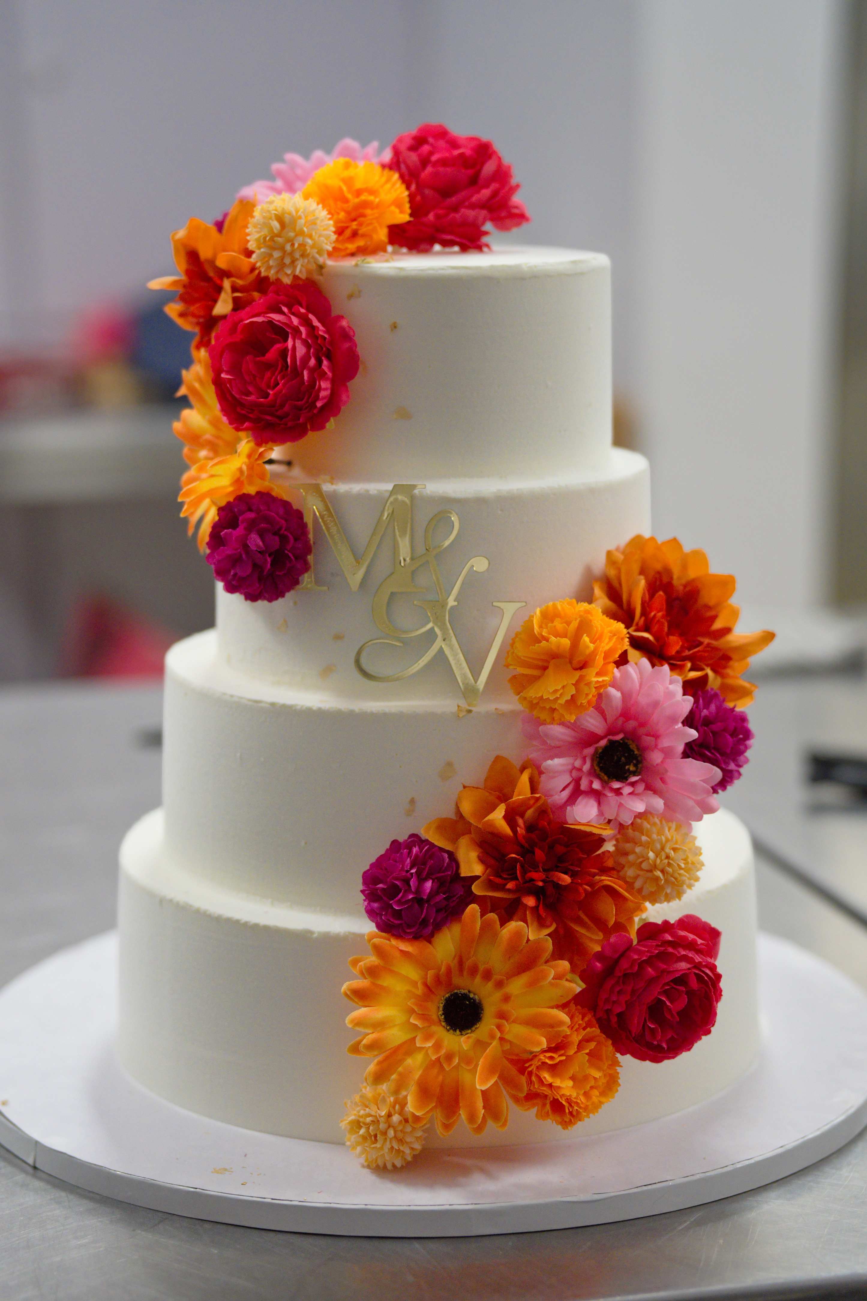 Gâteau blanc à quatre étages décoré de fleurs colorées orange, rose, rouge, et violet.