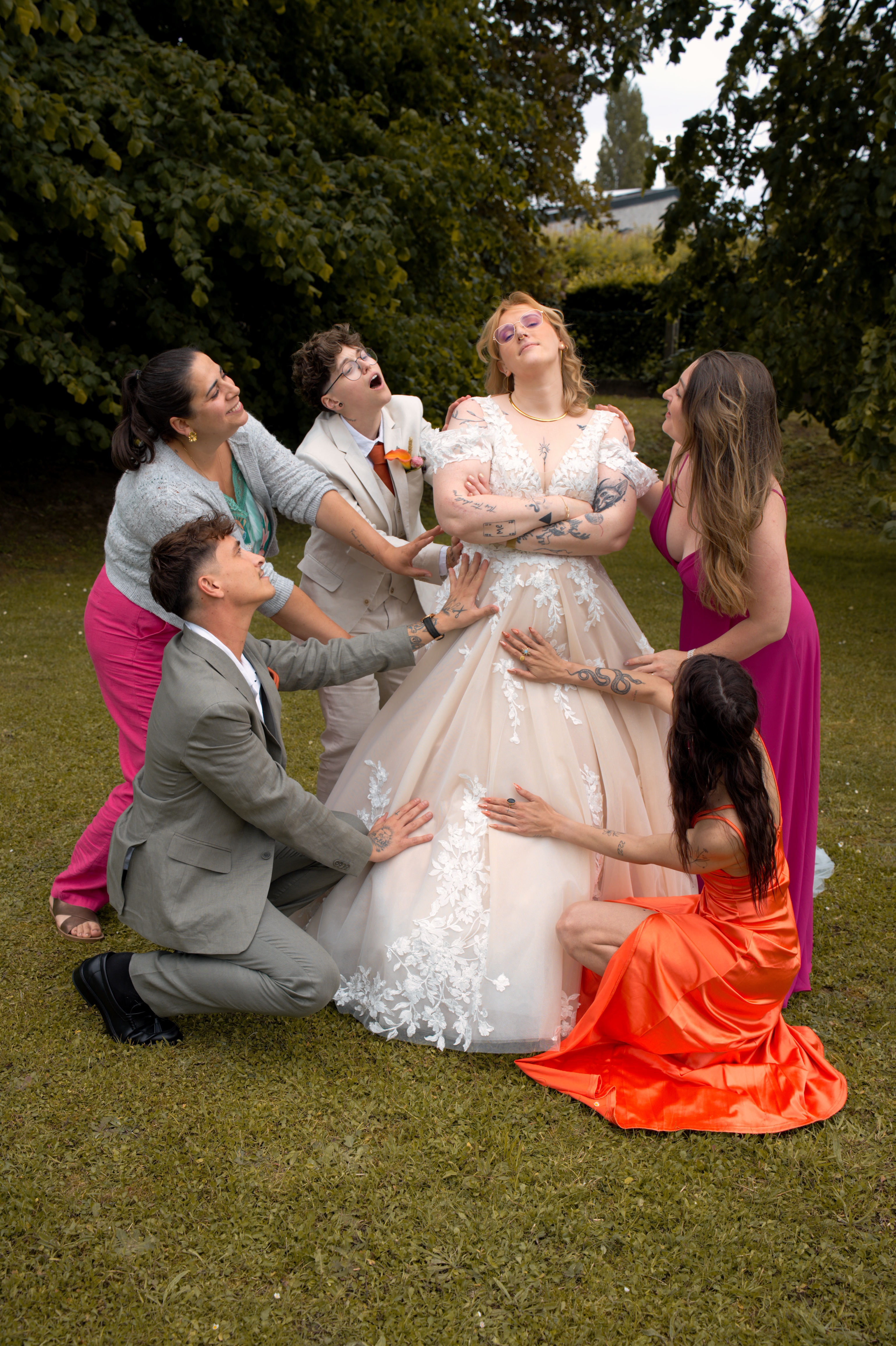 Cinq personnes touchant la robe d'une personne en robe de mariée blanche dans un jardin.