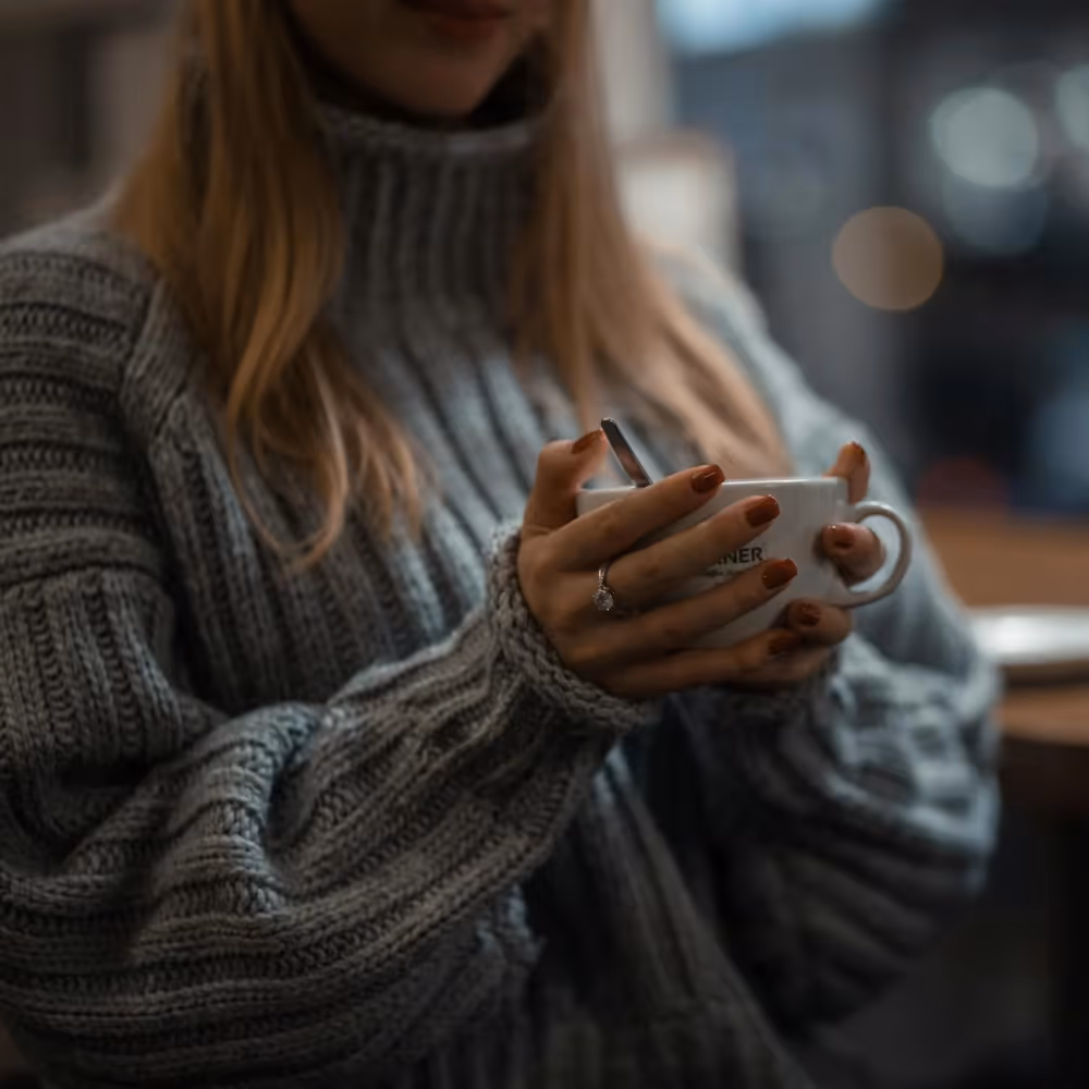 A woman in a chunky grey jumper holding a mug of coffee