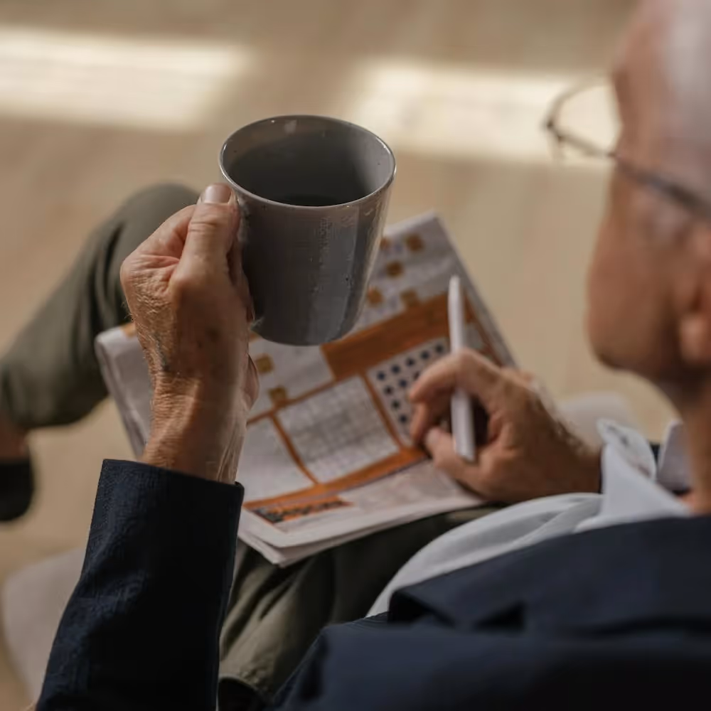 A man doing a crossword whilst holding a mug of tea