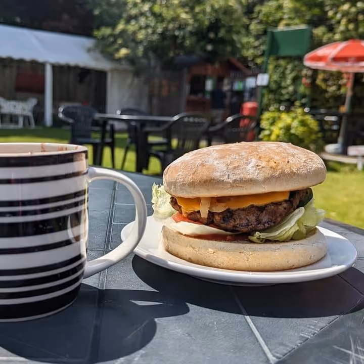 A burger in a bun and a mug of coffee on a table