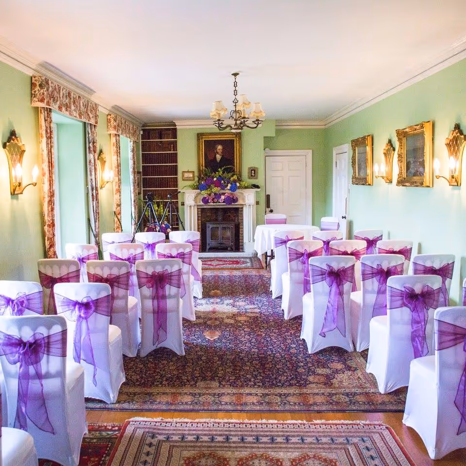 A room set up for wedding guests with purple bows on each chair
