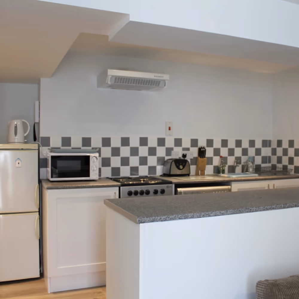 A white kitchen with grey worktop and checkerboard black and grey tiles