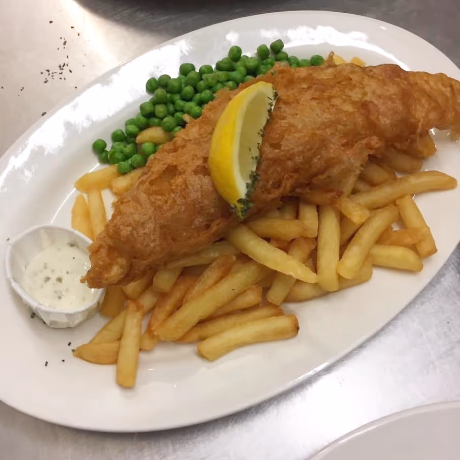 A plate of battered cod and chips with peas and tartar sauce