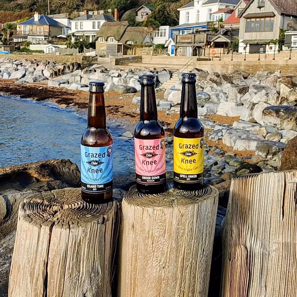 Three bottles of cider sitting upon wooden groins