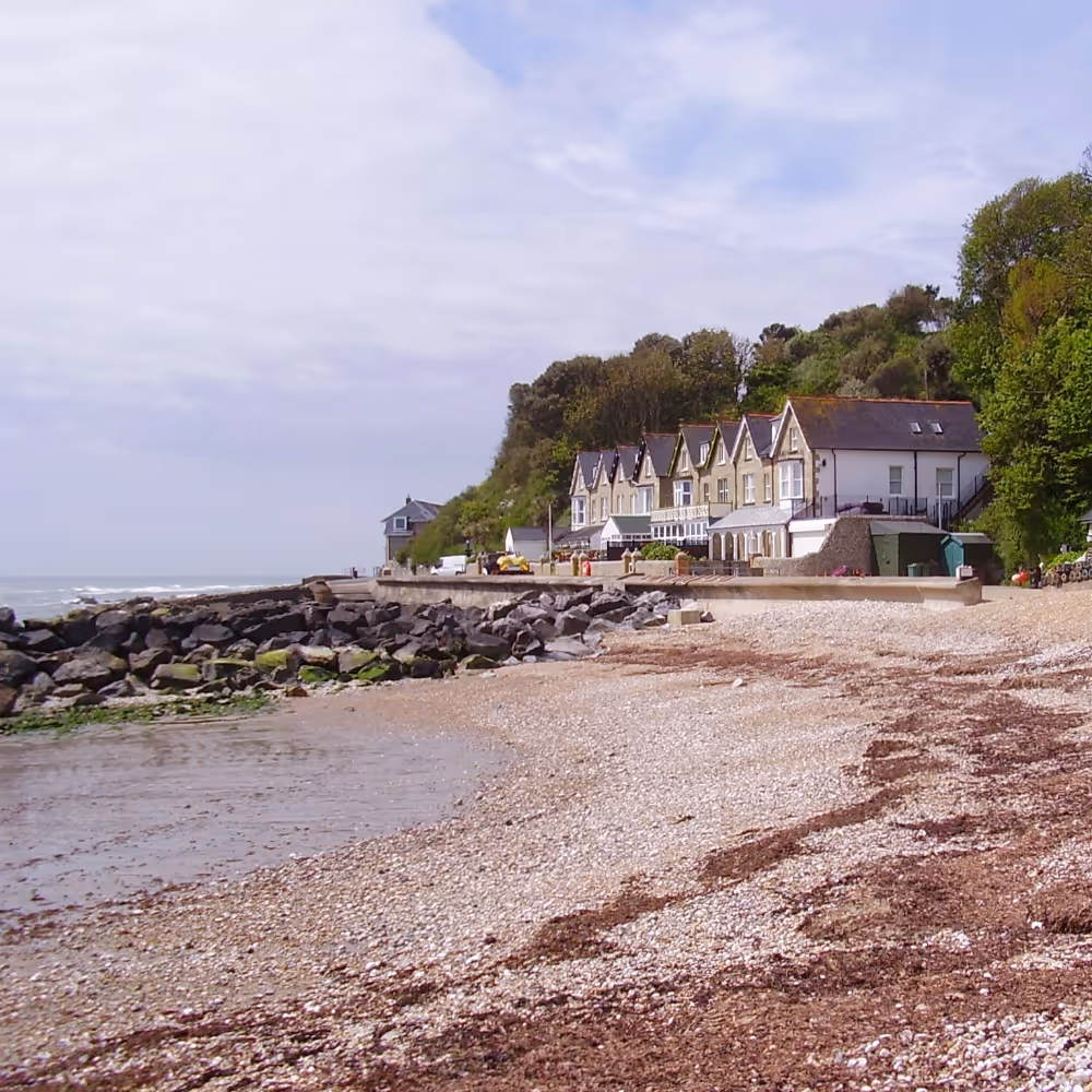 A small shingle beach with a row of houses in the distance